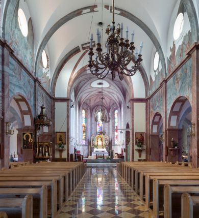 Zdjęcie nr 20: Trójnawowa, czteroprzęsłowa bazylika filarowa, z jednoprzęsłowym, zakończonym wielobocznie prezbiterium, przy którym od południa prostokątna zakrystia; od zachodu na osi wieża na rzucie kwadratu, z kruchtą w przyziemiu, częściowo wtopiona w korpus nawowy. Arkady międzynawowe i tęcza zamknięte półkoliście. Sklepienia kolebkowe z lunetami. Okna prostokątne zamknięte półkoliście, w nawie głównej, ponad arkadami międzynawowymi, okulusy. Fasada pięcioosiowa, pośrodku z ryzalitem wieży występującej przed lico elewacji nawy głównej i naw bocznych, w których zamknięte półkoliście otwory wejściowe. Wieża czterokondygnacyjna, nakryta ostrosłupowym, wysokim hełmem. Zakończenie prezbiterium opięte przyporami. Dachy dwuspadowe na nawą główną i prezbiterium, pulpitowe nad nawami bocznymi. 