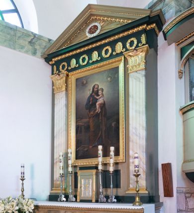 Zdjęcie nr 1: Nastawa architektoniczna, jednoosiowa, jednokondygnacyjna. Ołtarz drewniany, prostopadłościenny, na cokole, z malowaną płyciną na ściance przedniej w formie leżącego prostokąta o wklęsłych bokach, polichromowane na sposób imitujący marmoryzację w różnych odcieniach brązu, szarości i bieli. Zakończone profilowanym gzymsem, dekorowanym złoconym ornamentem roślinnym. Mensa drewniana. Na ołtarzu ustawione tabernakulum w formie drewnianej, prostopadłościennej skrzynki. Na przedniej ściance prostokątna płycina o owalnych narożach z przedstawieniem kielicha w glorii. Całość obwiedziona profilowanym, złoconym gzymsem. Na tabernakulum niski, prostopadłościenny tron wystawienia. Nastawa ujęta dwoma pilastrami o kanelowanych trzonach, dźwigających niepełne belkowanie i trójkątny przyczółek. Fryz dekorowany ustawionymi naprzemiennie anthemionami i wieńcami, belkowanie i przyczółek zdobione kimationem. W polu przyczółka owalny medalion z monogramem Chrystusa, ujęty wieńcem, w glorii promienistej. W polu środkowym obraz w formie stojącego prostokąta z wizerunkiem św. Józefa z Dzieciątkiem, ujęty profilowaną ramą dekorowaną kimationem. Nastawa polichromowana jest w kolorze szarym, trzony pilastrów są marmoryzowane, belkowanie o barwie zielono-niebieskiej. Profile, kapitele i dekoracja złocone, wieniec srebrzony. 