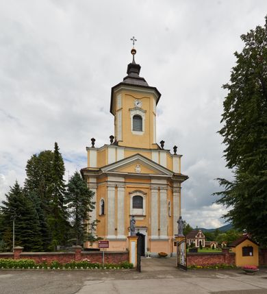 Zdjęcie nr 14: Kościół jest orientowany, murowany z cegły i kamienia, na rzucie podłużnym. Zajmuje powierzchnię około 606 metrów kwadratowych, długość bryły wynosi około 32, a szerokość 14 metrów. Jednonawowy, trójprzęsłowy korpus charakteryzuje środkowe, kwadratowe przęsło z płytkimi apsydami po bokach, wysuwającymi się przed lica elewacji bocznych, na wzór pseudotranseptu (para spłaszczonych apsyd). Przęsło wschodnie, na rzucie prostokąta, z wnękami po bokach, zakończone jest apsydą stanowiącą przestrzeń prezbiterium. Na osi kościoła i przedłużeniu prezbiterium jest piętrowa zakrystia ze skarbcem, natomiast w przedłużeniu przęsła zachodniego wieża ujęta po bokach piętrowymi lokalnościami. Korpus nawowy przekryty jest sklepieniem kolebkowym na gurtach, z lunetami, które w przęśle środkowym, na przecięciu z pseudotranseptem, tworzy rodzaj sklepienia krzyżowego z okrągłym zwierciadłem. Artykulację ścian wewnątrz kościoła stanowią pary pilastrów wspierające przerywane belkowanie. Na zewnątrz ściany korpusu, transeptu i zakrystii artykułują osadzone na niewysokim cokole lizeny wspierające obiegające całość belkowanie. Dodatkowo mury przeprute są owalnymi otworami okiennymi ujętymi profilowanymi obramieniami. Fasadę charakteryzuje w części środkowej ryzalit o skośnych ściankach bocznych oraz podziały podwójnymi i pojedynczymi pilastrami jońskimi, osadzonymi na wysokich cokołach i wspierającymi belkowanie. Do wnętrza kościoła prowadzą trzy otwory drzwiowe – w elewacji południowej, północnej i zachodniej. Drzwi w fasadzie są ujęte dekoracyjnym portalem z parą wąskich pilastrów, zwieńczonych zwężającymi się ku dołowi kapitelami, wspierających gzyms w formie łuku odcinkowego. Całość ujmuje obramienie o fantazyjnym wykroju w górnej partii, którego krawędzie obiega profilowana listwa z parą niewielkich wolut w górnych narożach. Obramienie drzwi wieńczy prosty gzyms odcinkowy nakryty blaszanym daszkiem. Po bokach wejścia znajduje się para kamiennych kropielnic. Powyżej otworu drzwiowego, pole środkowe fasady przeprute zostało oknem w kształcie stojącego prostokąta zamkniętego łukiem odcinkowym, zamurowanego w jednej trzeciej wysokości. Obramienie okna jest w formie pary pilastrów bez baz, wspierających fryz z kluczem pośrodku i parą wsporników wolutowych po bokach, dźwigających odcinkowy gzyms wieńczący. Pod parapetem umieszczono fartuch w kształcie leżącego prostokąta, o wklęsłych dolnych narożach, z dolną krawędzią zdobioną motywem lambrekinu. W skośnych ścianach bocznych ryzalitu znajduje się para zamkniętych półkoliście niszy z figurami św. Piotra po lewej i św. Pawła po prawej stronie. 
Ryzalit wieńczy trójkątny przyczółek z herbem Nowina w tympanonie. Nad belkowaniem, na całej szerokości fasady, znajduje się prosta attyka z odpowiadającymi dolnej strefie elewacji podziałami lizenowymi, wspierającymi wyłamujący się ponad nimi gzyms ozdobiony wazonami. Powyżej wznosi się górne piętro wieży, czworościenne o ściętych narożnikach, nakryte kopulastym hełmem z nasadnikiem.  
Północna, zachodnia i południowa ściana wieży przeprute są otworami okiennymi w kształcie stojącego prostokąta zamkniętego łukiem odcinkowym. Okna mają obramienia w kształcie stojących prostokątów z uszakami w górnych narożach, zwieńczone są belkowaniem w formie łuku odcinkowego z kluczem pośrodku i parą wolutowych wsporników po bokach fryzu. Podwieszenie ma formę fartucha w kształcie leżącego prostokąta o wklęsłych dolnych narożach i dolnej krawędzi zdobionej motywem lambrekinu. Powyżej otworów okiennych znajdują się okrągłe tarcze zegarowe. Pola ściętych naroży wieży zdobi ornamentyka cekinowa i kampanule. Korpus nawowy przykrywa dwuspadowy dach zakończony pięciopołaciowo nad prezbiterium i trójpołaciowo nad końcami transeptu, kryty dachówką. Na skrzyżowaniu korpusu nawowego i transeptu ulokowano obitą blachą wieżyczkę na sygnaturkę. Kolorystyka tynków kościoła utrzymana jest w odcieniu ugru, w dolnej partii różu, detal architektoniczny i ornamentyka w bieli. 

Plac przykościelny otoczony jest murowanym parkanem z usytuowanymi w nim 14 kapliczkami ze stacjami drogi krzyżowej, nakrytymi dwuspadowymi dachami. W jednym z naroży znajduje się niewielka, murowana kaplica grobowa rodziny Romerów o ceglanych ścianach artykułowanych białymi pilastrami i fasadzie ze szczytem ujętym parą spływów i zwieńczonym trójkątnym przyczółkiem.   
