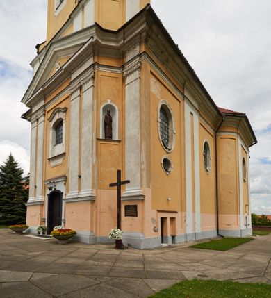 Zdjęcie nr 17: Kościół jest orientowany, murowany z cegły i kamienia, na rzucie podłużnym. Zajmuje powierzchnię około 606 metrów kwadratowych, długość bryły wynosi około 32, a szerokość 14 metrów. Jednonawowy, trójprzęsłowy korpus charakteryzuje środkowe, kwadratowe przęsło z płytkimi apsydami po bokach, wysuwającymi się przed lica elewacji bocznych, na wzór pseudotranseptu (para spłaszczonych apsyd). Przęsło wschodnie, na rzucie prostokąta, z wnękami po bokach, zakończone jest apsydą stanowiącą przestrzeń prezbiterium. Na osi kościoła i przedłużeniu prezbiterium jest piętrowa zakrystia ze skarbcem, natomiast w przedłużeniu przęsła zachodniego wieża ujęta po bokach piętrowymi lokalnościami. Korpus nawowy przekryty jest sklepieniem kolebkowym na gurtach, z lunetami, które w przęśle środkowym, na przecięciu z pseudotranseptem, tworzy rodzaj sklepienia krzyżowego z okrągłym zwierciadłem. Artykulację ścian wewnątrz kościoła stanowią pary pilastrów wspierające przerywane belkowanie. Na zewnątrz ściany korpusu, transeptu i zakrystii artykułują osadzone na niewysokim cokole lizeny wspierające obiegające całość belkowanie. Dodatkowo mury przeprute są owalnymi otworami okiennymi ujętymi profilowanymi obramieniami. Fasadę charakteryzuje w części środkowej ryzalit o skośnych ściankach bocznych oraz podziały podwójnymi i pojedynczymi pilastrami jońskimi, osadzonymi na wysokich cokołach i wspierającymi belkowanie. Do wnętrza kościoła prowadzą trzy otwory drzwiowe – w elewacji południowej, północnej i zachodniej. Drzwi w fasadzie są ujęte dekoracyjnym portalem z parą wąskich pilastrów, zwieńczonych zwężającymi się ku dołowi kapitelami, wspierających gzyms w formie łuku odcinkowego. Całość ujmuje obramienie o fantazyjnym wykroju w górnej partii, którego krawędzie obiega profilowana listwa z parą niewielkich wolut w górnych narożach. Obramienie drzwi wieńczy prosty gzyms odcinkowy nakryty blaszanym daszkiem. Po bokach wejścia znajduje się para kamiennych kropielnic. Powyżej otworu drzwiowego, pole środkowe fasady przeprute zostało oknem w kształcie stojącego prostokąta zamkniętego łukiem odcinkowym, zamurowanego w jednej trzeciej wysokości. Obramienie okna jest w formie pary pilastrów bez baz, wspierających fryz z kluczem pośrodku i parą wsporników wolutowych po bokach, dźwigających odcinkowy gzyms wieńczący. Pod parapetem umieszczono fartuch w kształcie leżącego prostokąta, o wklęsłych dolnych narożach, z dolną krawędzią zdobioną motywem lambrekinu. W skośnych ścianach bocznych ryzalitu znajduje się para zamkniętych półkoliście niszy z figurami św. Piotra po lewej i św. Pawła po prawej stronie. 
Ryzalit wieńczy trójkątny przyczółek z herbem Nowina w tympanonie. Nad belkowaniem, na całej szerokości fasady, znajduje się prosta attyka z odpowiadającymi dolnej strefie elewacji podziałami lizenowymi, wspierającymi wyłamujący się ponad nimi gzyms ozdobiony wazonami. Powyżej wznosi się górne piętro wieży, czworościenne o ściętych narożnikach, nakryte kopulastym hełmem z nasadnikiem.  
Północna, zachodnia i południowa ściana wieży przeprute są otworami okiennymi w kształcie stojącego prostokąta zamkniętego łukiem odcinkowym. Okna mają obramienia w kształcie stojących prostokątów z uszakami w górnych narożach, zwieńczone są belkowaniem w formie łuku odcinkowego z kluczem pośrodku i parą wolutowych wsporników po bokach fryzu. Podwieszenie ma formę fartucha w kształcie leżącego prostokąta o wklęsłych dolnych narożach i dolnej krawędzi zdobionej motywem lambrekinu. Powyżej otworów okiennych znajdują się okrągłe tarcze zegarowe. Pola ściętych naroży wieży zdobi ornamentyka cekinowa i kampanule. Korpus nawowy przykrywa dwuspadowy dach zakończony pięciopołaciowo nad prezbiterium i trójpołaciowo nad końcami transeptu, kryty dachówką. Na skrzyżowaniu korpusu nawowego i transeptu ulokowano obitą blachą wieżyczkę na sygnaturkę. Kolorystyka tynków kościoła utrzymana jest w odcieniu ugru, w dolnej partii różu, detal architektoniczny i ornamentyka w bieli. 

Plac przykościelny otoczony jest murowanym parkanem z usytuowanymi w nim 14 kapliczkami ze stacjami drogi krzyżowej, nakrytymi dwuspadowymi dachami. W jednym z naroży znajduje się niewielka, murowana kaplica grobowa rodziny Romerów o ceglanych ścianach artykułowanych białymi pilastrami i fasadzie ze szczytem ujętym parą spływów i zwieńczonym trójkątnym przyczółkiem.   
