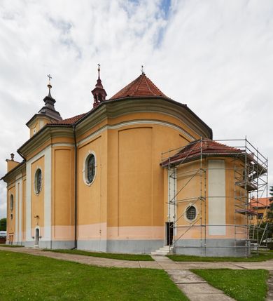 Zdjęcie nr 25: Kościół jest orientowany, murowany z cegły i kamienia, na rzucie podłużnym. Zajmuje powierzchnię około 606 metrów kwadratowych, długość bryły wynosi około 32, a szerokość 14 metrów. Jednonawowy, trójprzęsłowy korpus charakteryzuje środkowe, kwadratowe przęsło z płytkimi apsydami po bokach, wysuwającymi się przed lica elewacji bocznych, na wzór pseudotranseptu (para spłaszczonych apsyd). Przęsło wschodnie, na rzucie prostokąta, z wnękami po bokach, zakończone jest apsydą stanowiącą przestrzeń prezbiterium. Na osi kościoła i przedłużeniu prezbiterium jest piętrowa zakrystia ze skarbcem, natomiast w przedłużeniu przęsła zachodniego wieża ujęta po bokach piętrowymi lokalnościami. Korpus nawowy przekryty jest sklepieniem kolebkowym na gurtach, z lunetami, które w przęśle środkowym, na przecięciu z pseudotranseptem, tworzy rodzaj sklepienia krzyżowego z okrągłym zwierciadłem. Artykulację ścian wewnątrz kościoła stanowią pary pilastrów wspierające przerywane belkowanie. Na zewnątrz ściany korpusu, transeptu i zakrystii artykułują osadzone na niewysokim cokole lizeny wspierające obiegające całość belkowanie. Dodatkowo mury przeprute są owalnymi otworami okiennymi ujętymi profilowanymi obramieniami. Fasadę charakteryzuje w części środkowej ryzalit o skośnych ściankach bocznych oraz podziały podwójnymi i pojedynczymi pilastrami jońskimi, osadzonymi na wysokich cokołach i wspierającymi belkowanie. Do wnętrza kościoła prowadzą trzy otwory drzwiowe – w elewacji południowej, północnej i zachodniej. Drzwi w fasadzie są ujęte dekoracyjnym portalem z parą wąskich pilastrów, zwieńczonych zwężającymi się ku dołowi kapitelami, wspierających gzyms w formie łuku odcinkowego. Całość ujmuje obramienie o fantazyjnym wykroju w górnej partii, którego krawędzie obiega profilowana listwa z parą niewielkich wolut w górnych narożach. Obramienie drzwi wieńczy prosty gzyms odcinkowy nakryty blaszanym daszkiem. Po bokach wejścia znajduje się para kamiennych kropielnic. Powyżej otworu drzwiowego, pole środkowe fasady przeprute zostało oknem w kształcie stojącego prostokąta zamkniętego łukiem odcinkowym, zamurowanego w jednej trzeciej wysokości. Obramienie okna jest w formie pary pilastrów bez baz, wspierających fryz z kluczem pośrodku i parą wsporników wolutowych po bokach, dźwigających odcinkowy gzyms wieńczący. Pod parapetem umieszczono fartuch w kształcie leżącego prostokąta, o wklęsłych dolnych narożach, z dolną krawędzią zdobioną motywem lambrekinu. W skośnych ścianach bocznych ryzalitu znajduje się para zamkniętych półkoliście niszy z figurami św. Piotra po lewej i św. Pawła po prawej stronie. 
Ryzalit wieńczy trójkątny przyczółek z herbem Nowina w tympanonie. Nad belkowaniem, na całej szerokości fasady, znajduje się prosta attyka z odpowiadającymi dolnej strefie elewacji podziałami lizenowymi, wspierającymi wyłamujący się ponad nimi gzyms ozdobiony wazonami. Powyżej wznosi się górne piętro wieży, czworościenne o ściętych narożnikach, nakryte kopulastym hełmem z nasadnikiem.  
Północna, zachodnia i południowa ściana wieży przeprute są otworami okiennymi w kształcie stojącego prostokąta zamkniętego łukiem odcinkowym. Okna mają obramienia w kształcie stojących prostokątów z uszakami w górnych narożach, zwieńczone są belkowaniem w formie łuku odcinkowego z kluczem pośrodku i parą wolutowych wsporników po bokach fryzu. Podwieszenie ma formę fartucha w kształcie leżącego prostokąta o wklęsłych dolnych narożach i dolnej krawędzi zdobionej motywem lambrekinu. Powyżej otworów okiennych znajdują się okrągłe tarcze zegarowe. Pola ściętych naroży wieży zdobi ornamentyka cekinowa i kampanule. Korpus nawowy przykrywa dwuspadowy dach zakończony pięciopołaciowo nad prezbiterium i trójpołaciowo nad końcami transeptu, kryty dachówką. Na skrzyżowaniu korpusu nawowego i transeptu ulokowano obitą blachą wieżyczkę na sygnaturkę. Kolorystyka tynków kościoła utrzymana jest w odcieniu ugru, w dolnej partii różu, detal architektoniczny i ornamentyka w bieli. 

Plac przykościelny otoczony jest murowanym parkanem z usytuowanymi w nim 14 kapliczkami ze stacjami drogi krzyżowej, nakrytymi dwuspadowymi dachami. W jednym z naroży znajduje się niewielka, murowana kaplica grobowa rodziny Romerów o ceglanych ścianach artykułowanych białymi pilastrami i fasadzie ze szczytem ujętym parą spływów i zwieńczonym trójkątnym przyczółkiem.   
