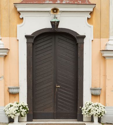 Zdjęcie nr 26: Kościół jest orientowany, murowany z cegły i kamienia, na rzucie podłużnym. Zajmuje powierzchnię około 606 metrów kwadratowych, długość bryły wynosi około 32, a szerokość 14 metrów. Jednonawowy, trójprzęsłowy korpus charakteryzuje środkowe, kwadratowe przęsło z płytkimi apsydami po bokach, wysuwającymi się przed lica elewacji bocznych, na wzór pseudotranseptu (para spłaszczonych apsyd). Przęsło wschodnie, na rzucie prostokąta, z wnękami po bokach, zakończone jest apsydą stanowiącą przestrzeń prezbiterium. Na osi kościoła i przedłużeniu prezbiterium jest piętrowa zakrystia ze skarbcem, natomiast w przedłużeniu przęsła zachodniego wieża ujęta po bokach piętrowymi lokalnościami. Korpus nawowy przekryty jest sklepieniem kolebkowym na gurtach, z lunetami, które w przęśle środkowym, na przecięciu z pseudotranseptem, tworzy rodzaj sklepienia krzyżowego z okrągłym zwierciadłem. Artykulację ścian wewnątrz kościoła stanowią pary pilastrów wspierające przerywane belkowanie. Na zewnątrz ściany korpusu, transeptu i zakrystii artykułują osadzone na niewysokim cokole lizeny wspierające obiegające całość belkowanie. Dodatkowo mury przeprute są owalnymi otworami okiennymi ujętymi profilowanymi obramieniami. Fasadę charakteryzuje w części środkowej ryzalit o skośnych ściankach bocznych oraz podziały podwójnymi i pojedynczymi pilastrami jońskimi, osadzonymi na wysokich cokołach i wspierającymi belkowanie. Do wnętrza kościoła prowadzą trzy otwory drzwiowe – w elewacji południowej, północnej i zachodniej. Drzwi w fasadzie są ujęte dekoracyjnym portalem z parą wąskich pilastrów, zwieńczonych zwężającymi się ku dołowi kapitelami, wspierających gzyms w formie łuku odcinkowego. Całość ujmuje obramienie o fantazyjnym wykroju w górnej partii, którego krawędzie obiega profilowana listwa z parą niewielkich wolut w górnych narożach. Obramienie drzwi wieńczy prosty gzyms odcinkowy nakryty blaszanym daszkiem. Po bokach wejścia znajduje się para kamiennych kropielnic. Powyżej otworu drzwiowego, pole środkowe fasady przeprute zostało oknem w kształcie stojącego prostokąta zamkniętego łukiem odcinkowym, zamurowanego w jednej trzeciej wysokości. Obramienie okna jest w formie pary pilastrów bez baz, wspierających fryz z kluczem pośrodku i parą wsporników wolutowych po bokach, dźwigających odcinkowy gzyms wieńczący. Pod parapetem umieszczono fartuch w kształcie leżącego prostokąta, o wklęsłych dolnych narożach, z dolną krawędzią zdobioną motywem lambrekinu. W skośnych ścianach bocznych ryzalitu znajduje się para zamkniętych półkoliście niszy z figurami św. Piotra po lewej i św. Pawła po prawej stronie. 
Ryzalit wieńczy trójkątny przyczółek z herbem Nowina w tympanonie. Nad belkowaniem, na całej szerokości fasady, znajduje się prosta attyka z odpowiadającymi dolnej strefie elewacji podziałami lizenowymi, wspierającymi wyłamujący się ponad nimi gzyms ozdobiony wazonami. Powyżej wznosi się górne piętro wieży, czworościenne o ściętych narożnikach, nakryte kopulastym hełmem z nasadnikiem.  
Północna, zachodnia i południowa ściana wieży przeprute są otworami okiennymi w kształcie stojącego prostokąta zamkniętego łukiem odcinkowym. Okna mają obramienia w kształcie stojących prostokątów z uszakami w górnych narożach, zwieńczone są belkowaniem w formie łuku odcinkowego z kluczem pośrodku i parą wolutowych wsporników po bokach fryzu. Podwieszenie ma formę fartucha w kształcie leżącego prostokąta o wklęsłych dolnych narożach i dolnej krawędzi zdobionej motywem lambrekinu. Powyżej otworów okiennych znajdują się okrągłe tarcze zegarowe. Pola ściętych naroży wieży zdobi ornamentyka cekinowa i kampanule. Korpus nawowy przykrywa dwuspadowy dach zakończony pięciopołaciowo nad prezbiterium i trójpołaciowo nad końcami transeptu, kryty dachówką. Na skrzyżowaniu korpusu nawowego i transeptu ulokowano obitą blachą wieżyczkę na sygnaturkę. Kolorystyka tynków kościoła utrzymana jest w odcieniu ugru, w dolnej partii różu, detal architektoniczny i ornamentyka w bieli. 

Plac przykościelny otoczony jest murowanym parkanem z usytuowanymi w nim 14 kapliczkami ze stacjami drogi krzyżowej, nakrytymi dwuspadowymi dachami. W jednym z naroży znajduje się niewielka, murowana kaplica grobowa rodziny Romerów o ceglanych ścianach artykułowanych białymi pilastrami i fasadzie ze szczytem ujętym parą spływów i zwieńczonym trójkątnym przyczółkiem.   
