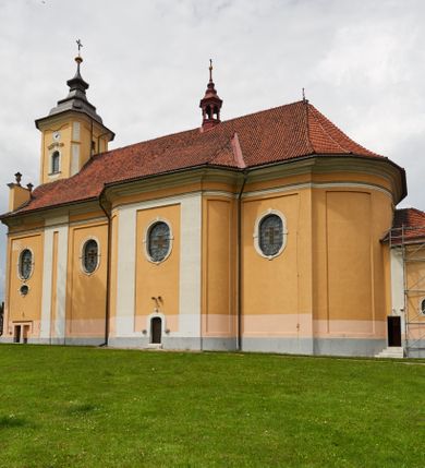 Zdjęcie nr 22: Kościół jest orientowany, murowany z cegły i kamienia, na rzucie podłużnym. Zajmuje powierzchnię około 606 metrów kwadratowych, długość bryły wynosi około 32, a szerokość 14 metrów. Jednonawowy, trójprzęsłowy korpus charakteryzuje środkowe, kwadratowe przęsło z płytkimi apsydami po bokach, wysuwającymi się przed lica elewacji bocznych, na wzór pseudotranseptu (para spłaszczonych apsyd). Przęsło wschodnie, na rzucie prostokąta, z wnękami po bokach, zakończone jest apsydą stanowiącą przestrzeń prezbiterium. Na osi kościoła i przedłużeniu prezbiterium jest piętrowa zakrystia ze skarbcem, natomiast w przedłużeniu przęsła zachodniego wieża ujęta po bokach piętrowymi lokalnościami. Korpus nawowy przekryty jest sklepieniem kolebkowym na gurtach, z lunetami, które w przęśle środkowym, na przecięciu z pseudotranseptem, tworzy rodzaj sklepienia krzyżowego z okrągłym zwierciadłem. Artykulację ścian wewnątrz kościoła stanowią pary pilastrów wspierające przerywane belkowanie. Na zewnątrz ściany korpusu, transeptu i zakrystii artykułują osadzone na niewysokim cokole lizeny wspierające obiegające całość belkowanie. Dodatkowo mury przeprute są owalnymi otworami okiennymi ujętymi profilowanymi obramieniami. Fasadę charakteryzuje w części środkowej ryzalit o skośnych ściankach bocznych oraz podziały podwójnymi i pojedynczymi pilastrami jońskimi, osadzonymi na wysokich cokołach i wspierającymi belkowanie. Do wnętrza kościoła prowadzą trzy otwory drzwiowe – w elewacji południowej, północnej i zachodniej. Drzwi w fasadzie są ujęte dekoracyjnym portalem z parą wąskich pilastrów, zwieńczonych zwężającymi się ku dołowi kapitelami, wspierających gzyms w formie łuku odcinkowego. Całość ujmuje obramienie o fantazyjnym wykroju w górnej partii, którego krawędzie obiega profilowana listwa z parą niewielkich wolut w górnych narożach. Obramienie drzwi wieńczy prosty gzyms odcinkowy nakryty blaszanym daszkiem. Po bokach wejścia znajduje się para kamiennych kropielnic. Powyżej otworu drzwiowego, pole środkowe fasady przeprute zostało oknem w kształcie stojącego prostokąta zamkniętego łukiem odcinkowym, zamurowanego w jednej trzeciej wysokości. Obramienie okna jest w formie pary pilastrów bez baz, wspierających fryz z kluczem pośrodku i parą wsporników wolutowych po bokach, dźwigających odcinkowy gzyms wieńczący. Pod parapetem umieszczono fartuch w kształcie leżącego prostokąta, o wklęsłych dolnych narożach, z dolną krawędzią zdobioną motywem lambrekinu. W skośnych ścianach bocznych ryzalitu znajduje się para zamkniętych półkoliście niszy z figurami św. Piotra po lewej i św. Pawła po prawej stronie. 
Ryzalit wieńczy trójkątny przyczółek z herbem Nowina w tympanonie. Nad belkowaniem, na całej szerokości fasady, znajduje się prosta attyka z odpowiadającymi dolnej strefie elewacji podziałami lizenowymi, wspierającymi wyłamujący się ponad nimi gzyms ozdobiony wazonami. Powyżej wznosi się górne piętro wieży, czworościenne o ściętych narożnikach, nakryte kopulastym hełmem z nasadnikiem.  
Północna, zachodnia i południowa ściana wieży przeprute są otworami okiennymi w kształcie stojącego prostokąta zamkniętego łukiem odcinkowym. Okna mają obramienia w kształcie stojących prostokątów z uszakami w górnych narożach, zwieńczone są belkowaniem w formie łuku odcinkowego z kluczem pośrodku i parą wolutowych wsporników po bokach fryzu. Podwieszenie ma formę fartucha w kształcie leżącego prostokąta o wklęsłych dolnych narożach i dolnej krawędzi zdobionej motywem lambrekinu. Powyżej otworów okiennych znajdują się okrągłe tarcze zegarowe. Pola ściętych naroży wieży zdobi ornamentyka cekinowa i kampanule. Korpus nawowy przykrywa dwuspadowy dach zakończony pięciopołaciowo nad prezbiterium i trójpołaciowo nad końcami transeptu, kryty dachówką. Na skrzyżowaniu korpusu nawowego i transeptu ulokowano obitą blachą wieżyczkę na sygnaturkę. Kolorystyka tynków kościoła utrzymana jest w odcieniu ugru, w dolnej partii różu, detal architektoniczny i ornamentyka w bieli. 

Plac przykościelny otoczony jest murowanym parkanem z usytuowanymi w nim 14 kapliczkami ze stacjami drogi krzyżowej, nakrytymi dwuspadowymi dachami. W jednym z naroży znajduje się niewielka, murowana kaplica grobowa rodziny Romerów o ceglanych ścianach artykułowanych białymi pilastrami i fasadzie ze szczytem ujętym parą spływów i zwieńczonym trójkątnym przyczółkiem.   
