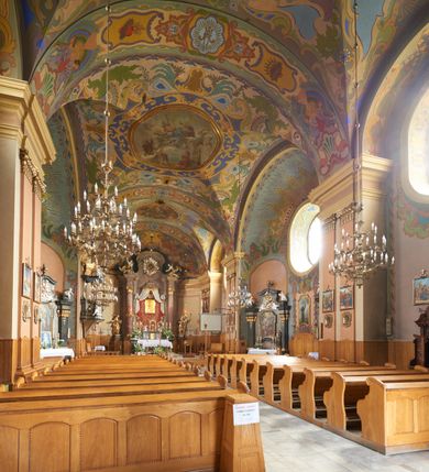 Zdjęcie nr 41: Kościół jest orientowany, murowany z cegły i kamienia, na rzucie podłużnym. Zajmuje powierzchnię około 606 metrów kwadratowych, długość bryły wynosi około 32, a szerokość 14 metrów. Jednonawowy, trójprzęsłowy korpus charakteryzuje środkowe, kwadratowe przęsło z płytkimi apsydami po bokach, wysuwającymi się przed lica elewacji bocznych, na wzór pseudotranseptu (para spłaszczonych apsyd). Przęsło wschodnie, na rzucie prostokąta, z wnękami po bokach, zakończone jest apsydą stanowiącą przestrzeń prezbiterium. Na osi kościoła i przedłużeniu prezbiterium jest piętrowa zakrystia ze skarbcem, natomiast w przedłużeniu przęsła zachodniego wieża ujęta po bokach piętrowymi lokalnościami. Korpus nawowy przekryty jest sklepieniem kolebkowym na gurtach, z lunetami, które w przęśle środkowym, na przecięciu z pseudotranseptem, tworzy rodzaj sklepienia krzyżowego z okrągłym zwierciadłem. Artykulację ścian wewnątrz kościoła stanowią pary pilastrów wspierające przerywane belkowanie. Na zewnątrz ściany korpusu, transeptu i zakrystii artykułują osadzone na niewysokim cokole lizeny wspierające obiegające całość belkowanie. Dodatkowo mury przeprute są owalnymi otworami okiennymi ujętymi profilowanymi obramieniami. Fasadę charakteryzuje w części środkowej ryzalit o skośnych ściankach bocznych oraz podziały podwójnymi i pojedynczymi pilastrami jońskimi, osadzonymi na wysokich cokołach i wspierającymi belkowanie. Do wnętrza kościoła prowadzą trzy otwory drzwiowe – w elewacji południowej, północnej i zachodniej. Drzwi w fasadzie są ujęte dekoracyjnym portalem z parą wąskich pilastrów, zwieńczonych zwężającymi się ku dołowi kapitelami, wspierających gzyms w formie łuku odcinkowego. Całość ujmuje obramienie o fantazyjnym wykroju w górnej partii, którego krawędzie obiega profilowana listwa z parą niewielkich wolut w górnych narożach. Obramienie drzwi wieńczy prosty gzyms odcinkowy nakryty blaszanym daszkiem. Po bokach wejścia znajduje się para kamiennych kropielnic. Powyżej otworu drzwiowego, pole środkowe fasady przeprute zostało oknem w kształcie stojącego prostokąta zamkniętego łukiem odcinkowym, zamurowanego w jednej trzeciej wysokości. Obramienie okna jest w formie pary pilastrów bez baz, wspierających fryz z kluczem pośrodku i parą wsporników wolutowych po bokach, dźwigających odcinkowy gzyms wieńczący. Pod parapetem umieszczono fartuch w kształcie leżącego prostokąta, o wklęsłych dolnych narożach, z dolną krawędzią zdobioną motywem lambrekinu. W skośnych ścianach bocznych ryzalitu znajduje się para zamkniętych półkoliście niszy z figurami św. Piotra po lewej i św. Pawła po prawej stronie. 
Ryzalit wieńczy trójkątny przyczółek z herbem Nowina w tympanonie. Nad belkowaniem, na całej szerokości fasady, znajduje się prosta attyka z odpowiadającymi dolnej strefie elewacji podziałami lizenowymi, wspierającymi wyłamujący się ponad nimi gzyms ozdobiony wazonami. Powyżej wznosi się górne piętro wieży, czworościenne o ściętych narożnikach, nakryte kopulastym hełmem z nasadnikiem.  
Północna, zachodnia i południowa ściana wieży przeprute są otworami okiennymi w kształcie stojącego prostokąta zamkniętego łukiem odcinkowym. Okna mają obramienia w kształcie stojących prostokątów z uszakami w górnych narożach, zwieńczone są belkowaniem w formie łuku odcinkowego z kluczem pośrodku i parą wolutowych wsporników po bokach fryzu. Podwieszenie ma formę fartucha w kształcie leżącego prostokąta o wklęsłych dolnych narożach i dolnej krawędzi zdobionej motywem lambrekinu. Powyżej otworów okiennych znajdują się okrągłe tarcze zegarowe. Pola ściętych naroży wieży zdobi ornamentyka cekinowa i kampanule. Korpus nawowy przykrywa dwuspadowy dach zakończony pięciopołaciowo nad prezbiterium i trójpołaciowo nad końcami transeptu, kryty dachówką. Na skrzyżowaniu korpusu nawowego i transeptu ulokowano obitą blachą wieżyczkę na sygnaturkę. Kolorystyka tynków kościoła utrzymana jest w odcieniu ugru, w dolnej partii różu, detal architektoniczny i ornamentyka w bieli. 

Plac przykościelny otoczony jest murowanym parkanem z usytuowanymi w nim 14 kapliczkami ze stacjami drogi krzyżowej, nakrytymi dwuspadowymi dachami. W jednym z naroży znajduje się niewielka, murowana kaplica grobowa rodziny Romerów o ceglanych ścianach artykułowanych białymi pilastrami i fasadzie ze szczytem ujętym parą spływów i zwieńczonym trójkątnym przyczółkiem.   
