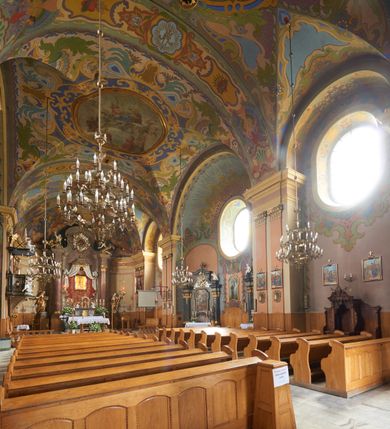 Zdjęcie nr 2: Kościół jest orientowany, murowany z cegły i kamienia, na rzucie podłużnym. Zajmuje powierzchnię około 606 metrów kwadratowych, długość bryły wynosi około 32, a szerokość 14 metrów. Jednonawowy, trójprzęsłowy korpus charakteryzuje środkowe, kwadratowe przęsło z płytkimi apsydami po bokach, wysuwającymi się przed lica elewacji bocznych, na wzór pseudotranseptu (para spłaszczonych apsyd). Przęsło wschodnie, na rzucie prostokąta, z wnękami po bokach, zakończone jest apsydą stanowiącą przestrzeń prezbiterium. Na osi kościoła i przedłużeniu prezbiterium jest piętrowa zakrystia ze skarbcem, natomiast w przedłużeniu przęsła zachodniego wieża ujęta po bokach piętrowymi lokalnościami. Korpus nawowy przekryty jest sklepieniem kolebkowym na gurtach, z lunetami, które w przęśle środkowym, na przecięciu z pseudotranseptem, tworzy rodzaj sklepienia krzyżowego z okrągłym zwierciadłem. Artykulację ścian wewnątrz kościoła stanowią pary pilastrów wspierające przerywane belkowanie. Na zewnątrz ściany korpusu, transeptu i zakrystii artykułują osadzone na niewysokim cokole lizeny wspierające obiegające całość belkowanie. Dodatkowo mury przeprute są owalnymi otworami okiennymi ujętymi profilowanymi obramieniami. Fasadę charakteryzuje w części środkowej ryzalit o skośnych ściankach bocznych oraz podziały podwójnymi i pojedynczymi pilastrami jońskimi, osadzonymi na wysokich cokołach i wspierającymi belkowanie. Do wnętrza kościoła prowadzą trzy otwory drzwiowe – w elewacji południowej, północnej i zachodniej. Drzwi w fasadzie są ujęte dekoracyjnym portalem z parą wąskich pilastrów, zwieńczonych zwężającymi się ku dołowi kapitelami, wspierających gzyms w formie łuku odcinkowego. Całość ujmuje obramienie o fantazyjnym wykroju w górnej partii, którego krawędzie obiega profilowana listwa z parą niewielkich wolut w górnych narożach. Obramienie drzwi wieńczy prosty gzyms odcinkowy nakryty blaszanym daszkiem. Po bokach wejścia znajduje się para kamiennych kropielnic. Powyżej otworu drzwiowego, pole środkowe fasady przeprute zostało oknem w kształcie stojącego prostokąta zamkniętego łukiem odcinkowym, zamurowanego w jednej trzeciej wysokości. Obramienie okna jest w formie pary pilastrów bez baz, wspierających fryz z kluczem pośrodku i parą wsporników wolutowych po bokach, dźwigających odcinkowy gzyms wieńczący. Pod parapetem umieszczono fartuch w kształcie leżącego prostokąta, o wklęsłych dolnych narożach, z dolną krawędzią zdobioną motywem lambrekinu. W skośnych ścianach bocznych ryzalitu znajduje się para zamkniętych półkoliście niszy z figurami św. Piotra po lewej i św. Pawła po prawej stronie. 
Ryzalit wieńczy trójkątny przyczółek z herbem Nowina w tympanonie. Nad belkowaniem, na całej szerokości fasady, znajduje się prosta attyka z odpowiadającymi dolnej strefie elewacji podziałami lizenowymi, wspierającymi wyłamujący się ponad nimi gzyms ozdobiony wazonami. Powyżej wznosi się górne piętro wieży, czworościenne o ściętych narożnikach, nakryte kopulastym hełmem z nasadnikiem.  
Północna, zachodnia i południowa ściana wieży przeprute są otworami okiennymi w kształcie stojącego prostokąta zamkniętego łukiem odcinkowym. Okna mają obramienia w kształcie stojących prostokątów z uszakami w górnych narożach, zwieńczone są belkowaniem w formie łuku odcinkowego z kluczem pośrodku i parą wolutowych wsporników po bokach fryzu. Podwieszenie ma formę fartucha w kształcie leżącego prostokąta o wklęsłych dolnych narożach i dolnej krawędzi zdobionej motywem lambrekinu. Powyżej otworów okiennych znajdują się okrągłe tarcze zegarowe. Pola ściętych naroży wieży zdobi ornamentyka cekinowa i kampanule. Korpus nawowy przykrywa dwuspadowy dach zakończony pięciopołaciowo nad prezbiterium i trójpołaciowo nad końcami transeptu, kryty dachówką. Na skrzyżowaniu korpusu nawowego i transeptu ulokowano obitą blachą wieżyczkę na sygnaturkę. Kolorystyka tynków kościoła utrzymana jest w odcieniu ugru, w dolnej partii różu, detal architektoniczny i ornamentyka w bieli. 

Plac przykościelny otoczony jest murowanym parkanem z usytuowanymi w nim 14 kapliczkami ze stacjami drogi krzyżowej, nakrytymi dwuspadowymi dachami. W jednym z naroży znajduje się niewielka, murowana kaplica grobowa rodziny Romerów o ceglanych ścianach artykułowanych białymi pilastrami i fasadzie ze szczytem ujętym parą spływów i zwieńczonym trójkątnym przyczółkiem.   
