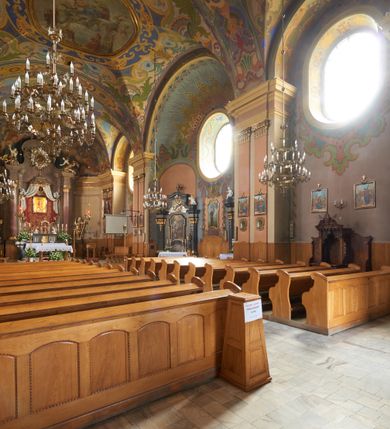 Zdjęcie nr 4: Kościół jest orientowany, murowany z cegły i kamienia, na rzucie podłużnym. Zajmuje powierzchnię około 606 metrów kwadratowych, długość bryły wynosi około 32, a szerokość 14 metrów. Jednonawowy, trójprzęsłowy korpus charakteryzuje środkowe, kwadratowe przęsło z płytkimi apsydami po bokach, wysuwającymi się przed lica elewacji bocznych, na wzór pseudotranseptu (para spłaszczonych apsyd). Przęsło wschodnie, na rzucie prostokąta, z wnękami po bokach, zakończone jest apsydą stanowiącą przestrzeń prezbiterium. Na osi kościoła i przedłużeniu prezbiterium jest piętrowa zakrystia ze skarbcem, natomiast w przedłużeniu przęsła zachodniego wieża ujęta po bokach piętrowymi lokalnościami. Korpus nawowy przekryty jest sklepieniem kolebkowym na gurtach, z lunetami, które w przęśle środkowym, na przecięciu z pseudotranseptem, tworzy rodzaj sklepienia krzyżowego z okrągłym zwierciadłem. Artykulację ścian wewnątrz kościoła stanowią pary pilastrów wspierające przerywane belkowanie. Na zewnątrz ściany korpusu, transeptu i zakrystii artykułują osadzone na niewysokim cokole lizeny wspierające obiegające całość belkowanie. Dodatkowo mury przeprute są owalnymi otworami okiennymi ujętymi profilowanymi obramieniami. Fasadę charakteryzuje w części środkowej ryzalit o skośnych ściankach bocznych oraz podziały podwójnymi i pojedynczymi pilastrami jońskimi, osadzonymi na wysokich cokołach i wspierającymi belkowanie. Do wnętrza kościoła prowadzą trzy otwory drzwiowe – w elewacji południowej, północnej i zachodniej. Drzwi w fasadzie są ujęte dekoracyjnym portalem z parą wąskich pilastrów, zwieńczonych zwężającymi się ku dołowi kapitelami, wspierających gzyms w formie łuku odcinkowego. Całość ujmuje obramienie o fantazyjnym wykroju w górnej partii, którego krawędzie obiega profilowana listwa z parą niewielkich wolut w górnych narożach. Obramienie drzwi wieńczy prosty gzyms odcinkowy nakryty blaszanym daszkiem. Po bokach wejścia znajduje się para kamiennych kropielnic. Powyżej otworu drzwiowego, pole środkowe fasady przeprute zostało oknem w kształcie stojącego prostokąta zamkniętego łukiem odcinkowym, zamurowanego w jednej trzeciej wysokości. Obramienie okna jest w formie pary pilastrów bez baz, wspierających fryz z kluczem pośrodku i parą wsporników wolutowych po bokach, dźwigających odcinkowy gzyms wieńczący. Pod parapetem umieszczono fartuch w kształcie leżącego prostokąta, o wklęsłych dolnych narożach, z dolną krawędzią zdobioną motywem lambrekinu. W skośnych ścianach bocznych ryzalitu znajduje się para zamkniętych półkoliście niszy z figurami św. Piotra po lewej i św. Pawła po prawej stronie. 
Ryzalit wieńczy trójkątny przyczółek z herbem Nowina w tympanonie. Nad belkowaniem, na całej szerokości fasady, znajduje się prosta attyka z odpowiadającymi dolnej strefie elewacji podziałami lizenowymi, wspierającymi wyłamujący się ponad nimi gzyms ozdobiony wazonami. Powyżej wznosi się górne piętro wieży, czworościenne o ściętych narożnikach, nakryte kopulastym hełmem z nasadnikiem.  
Północna, zachodnia i południowa ściana wieży przeprute są otworami okiennymi w kształcie stojącego prostokąta zamkniętego łukiem odcinkowym. Okna mają obramienia w kształcie stojących prostokątów z uszakami w górnych narożach, zwieńczone są belkowaniem w formie łuku odcinkowego z kluczem pośrodku i parą wolutowych wsporników po bokach fryzu. Podwieszenie ma formę fartucha w kształcie leżącego prostokąta o wklęsłych dolnych narożach i dolnej krawędzi zdobionej motywem lambrekinu. Powyżej otworów okiennych znajdują się okrągłe tarcze zegarowe. Pola ściętych naroży wieży zdobi ornamentyka cekinowa i kampanule. Korpus nawowy przykrywa dwuspadowy dach zakończony pięciopołaciowo nad prezbiterium i trójpołaciowo nad końcami transeptu, kryty dachówką. Na skrzyżowaniu korpusu nawowego i transeptu ulokowano obitą blachą wieżyczkę na sygnaturkę. Kolorystyka tynków kościoła utrzymana jest w odcieniu ugru, w dolnej partii różu, detal architektoniczny i ornamentyka w bieli. 

Plac przykościelny otoczony jest murowanym parkanem z usytuowanymi w nim 14 kapliczkami ze stacjami drogi krzyżowej, nakrytymi dwuspadowymi dachami. W jednym z naroży znajduje się niewielka, murowana kaplica grobowa rodziny Romerów o ceglanych ścianach artykułowanych białymi pilastrami i fasadzie ze szczytem ujętym parą spływów i zwieńczonym trójkątnym przyczółkiem.   
