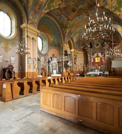 Zdjęcie nr 6: Kościół jest orientowany, murowany z cegły i kamienia, na rzucie podłużnym. Zajmuje powierzchnię około 606 metrów kwadratowych, długość bryły wynosi około 32, a szerokość 14 metrów. Jednonawowy, trójprzęsłowy korpus charakteryzuje środkowe, kwadratowe przęsło z płytkimi apsydami po bokach, wysuwającymi się przed lica elewacji bocznych, na wzór pseudotranseptu (para spłaszczonych apsyd). Przęsło wschodnie, na rzucie prostokąta, z wnękami po bokach, zakończone jest apsydą stanowiącą przestrzeń prezbiterium. Na osi kościoła i przedłużeniu prezbiterium jest piętrowa zakrystia ze skarbcem, natomiast w przedłużeniu przęsła zachodniego wieża ujęta po bokach piętrowymi lokalnościami. Korpus nawowy przekryty jest sklepieniem kolebkowym na gurtach, z lunetami, które w przęśle środkowym, na przecięciu z pseudotranseptem, tworzy rodzaj sklepienia krzyżowego z okrągłym zwierciadłem. Artykulację ścian wewnątrz kościoła stanowią pary pilastrów wspierające przerywane belkowanie. Na zewnątrz ściany korpusu, transeptu i zakrystii artykułują osadzone na niewysokim cokole lizeny wspierające obiegające całość belkowanie. Dodatkowo mury przeprute są owalnymi otworami okiennymi ujętymi profilowanymi obramieniami. Fasadę charakteryzuje w części środkowej ryzalit o skośnych ściankach bocznych oraz podziały podwójnymi i pojedynczymi pilastrami jońskimi, osadzonymi na wysokich cokołach i wspierającymi belkowanie. Do wnętrza kościoła prowadzą trzy otwory drzwiowe – w elewacji południowej, północnej i zachodniej. Drzwi w fasadzie są ujęte dekoracyjnym portalem z parą wąskich pilastrów, zwieńczonych zwężającymi się ku dołowi kapitelami, wspierających gzyms w formie łuku odcinkowego. Całość ujmuje obramienie o fantazyjnym wykroju w górnej partii, którego krawędzie obiega profilowana listwa z parą niewielkich wolut w górnych narożach. Obramienie drzwi wieńczy prosty gzyms odcinkowy nakryty blaszanym daszkiem. Po bokach wejścia znajduje się para kamiennych kropielnic. Powyżej otworu drzwiowego, pole środkowe fasady przeprute zostało oknem w kształcie stojącego prostokąta zamkniętego łukiem odcinkowym, zamurowanego w jednej trzeciej wysokości. Obramienie okna jest w formie pary pilastrów bez baz, wspierających fryz z kluczem pośrodku i parą wsporników wolutowych po bokach, dźwigających odcinkowy gzyms wieńczący. Pod parapetem umieszczono fartuch w kształcie leżącego prostokąta, o wklęsłych dolnych narożach, z dolną krawędzią zdobioną motywem lambrekinu. W skośnych ścianach bocznych ryzalitu znajduje się para zamkniętych półkoliście niszy z figurami św. Piotra po lewej i św. Pawła po prawej stronie. 
Ryzalit wieńczy trójkątny przyczółek z herbem Nowina w tympanonie. Nad belkowaniem, na całej szerokości fasady, znajduje się prosta attyka z odpowiadającymi dolnej strefie elewacji podziałami lizenowymi, wspierającymi wyłamujący się ponad nimi gzyms ozdobiony wazonami. Powyżej wznosi się górne piętro wieży, czworościenne o ściętych narożnikach, nakryte kopulastym hełmem z nasadnikiem.  
Północna, zachodnia i południowa ściana wieży przeprute są otworami okiennymi w kształcie stojącego prostokąta zamkniętego łukiem odcinkowym. Okna mają obramienia w kształcie stojących prostokątów z uszakami w górnych narożach, zwieńczone są belkowaniem w formie łuku odcinkowego z kluczem pośrodku i parą wolutowych wsporników po bokach fryzu. Podwieszenie ma formę fartucha w kształcie leżącego prostokąta o wklęsłych dolnych narożach i dolnej krawędzi zdobionej motywem lambrekinu. Powyżej otworów okiennych znajdują się okrągłe tarcze zegarowe. Pola ściętych naroży wieży zdobi ornamentyka cekinowa i kampanule. Korpus nawowy przykrywa dwuspadowy dach zakończony pięciopołaciowo nad prezbiterium i trójpołaciowo nad końcami transeptu, kryty dachówką. Na skrzyżowaniu korpusu nawowego i transeptu ulokowano obitą blachą wieżyczkę na sygnaturkę. Kolorystyka tynków kościoła utrzymana jest w odcieniu ugru, w dolnej partii różu, detal architektoniczny i ornamentyka w bieli. 

Plac przykościelny otoczony jest murowanym parkanem z usytuowanymi w nim 14 kapliczkami ze stacjami drogi krzyżowej, nakrytymi dwuspadowymi dachami. W jednym z naroży znajduje się niewielka, murowana kaplica grobowa rodziny Romerów o ceglanych ścianach artykułowanych białymi pilastrami i fasadzie ze szczytem ujętym parą spływów i zwieńczonym trójkątnym przyczółkiem.   
