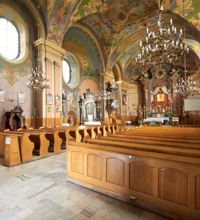 Zdjęcie nr 7: Kościół jest orientowany, murowany z cegły i kamienia, na rzucie podłużnym. Zajmuje powierzchnię około 606 metrów kwadratowych, długość bryły wynosi około 32, a szerokość 14 metrów. Jednonawowy, trójprzęsłowy korpus charakteryzuje środkowe, kwadratowe przęsło z płytkimi apsydami po bokach, wysuwającymi się przed lica elewacji bocznych, na wzór pseudotranseptu (para spłaszczonych apsyd). Przęsło wschodnie, na rzucie prostokąta, z wnękami po bokach, zakończone jest apsydą stanowiącą przestrzeń prezbiterium. Na osi kościoła i przedłużeniu prezbiterium jest piętrowa zakrystia ze skarbcem, natomiast w przedłużeniu przęsła zachodniego wieża ujęta po bokach piętrowymi lokalnościami. Korpus nawowy przekryty jest sklepieniem kolebkowym na gurtach, z lunetami, które w przęśle środkowym, na przecięciu z pseudotranseptem, tworzy rodzaj sklepienia krzyżowego z okrągłym zwierciadłem. Artykulację ścian wewnątrz kościoła stanowią pary pilastrów wspierające przerywane belkowanie. Na zewnątrz ściany korpusu, transeptu i zakrystii artykułują osadzone na niewysokim cokole lizeny wspierające obiegające całość belkowanie. Dodatkowo mury przeprute są owalnymi otworami okiennymi ujętymi profilowanymi obramieniami. Fasadę charakteryzuje w części środkowej ryzalit o skośnych ściankach bocznych oraz podziały podwójnymi i pojedynczymi pilastrami jońskimi, osadzonymi na wysokich cokołach i wspierającymi belkowanie. Do wnętrza kościoła prowadzą trzy otwory drzwiowe – w elewacji południowej, północnej i zachodniej. Drzwi w fasadzie są ujęte dekoracyjnym portalem z parą wąskich pilastrów, zwieńczonych zwężającymi się ku dołowi kapitelami, wspierających gzyms w formie łuku odcinkowego. Całość ujmuje obramienie o fantazyjnym wykroju w górnej partii, którego krawędzie obiega profilowana listwa z parą niewielkich wolut w górnych narożach. Obramienie drzwi wieńczy prosty gzyms odcinkowy nakryty blaszanym daszkiem. Po bokach wejścia znajduje się para kamiennych kropielnic. Powyżej otworu drzwiowego, pole środkowe fasady przeprute zostało oknem w kształcie stojącego prostokąta zamkniętego łukiem odcinkowym, zamurowanego w jednej trzeciej wysokości. Obramienie okna jest w formie pary pilastrów bez baz, wspierających fryz z kluczem pośrodku i parą wsporników wolutowych po bokach, dźwigających odcinkowy gzyms wieńczący. Pod parapetem umieszczono fartuch w kształcie leżącego prostokąta, o wklęsłych dolnych narożach, z dolną krawędzią zdobioną motywem lambrekinu. W skośnych ścianach bocznych ryzalitu znajduje się para zamkniętych półkoliście niszy z figurami św. Piotra po lewej i św. Pawła po prawej stronie. 
Ryzalit wieńczy trójkątny przyczółek z herbem Nowina w tympanonie. Nad belkowaniem, na całej szerokości fasady, znajduje się prosta attyka z odpowiadającymi dolnej strefie elewacji podziałami lizenowymi, wspierającymi wyłamujący się ponad nimi gzyms ozdobiony wazonami. Powyżej wznosi się górne piętro wieży, czworościenne o ściętych narożnikach, nakryte kopulastym hełmem z nasadnikiem.  
Północna, zachodnia i południowa ściana wieży przeprute są otworami okiennymi w kształcie stojącego prostokąta zamkniętego łukiem odcinkowym. Okna mają obramienia w kształcie stojących prostokątów z uszakami w górnych narożach, zwieńczone są belkowaniem w formie łuku odcinkowego z kluczem pośrodku i parą wolutowych wsporników po bokach fryzu. Podwieszenie ma formę fartucha w kształcie leżącego prostokąta o wklęsłych dolnych narożach i dolnej krawędzi zdobionej motywem lambrekinu. Powyżej otworów okiennych znajdują się okrągłe tarcze zegarowe. Pola ściętych naroży wieży zdobi ornamentyka cekinowa i kampanule. Korpus nawowy przykrywa dwuspadowy dach zakończony pięciopołaciowo nad prezbiterium i trójpołaciowo nad końcami transeptu, kryty dachówką. Na skrzyżowaniu korpusu nawowego i transeptu ulokowano obitą blachą wieżyczkę na sygnaturkę. Kolorystyka tynków kościoła utrzymana jest w odcieniu ugru, w dolnej partii różu, detal architektoniczny i ornamentyka w bieli. 

Plac przykościelny otoczony jest murowanym parkanem z usytuowanymi w nim 14 kapliczkami ze stacjami drogi krzyżowej, nakrytymi dwuspadowymi dachami. W jednym z naroży znajduje się niewielka, murowana kaplica grobowa rodziny Romerów o ceglanych ścianach artykułowanych białymi pilastrami i fasadzie ze szczytem ujętym parą spływów i zwieńczonym trójkątnym przyczółkiem.   
