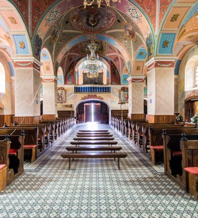 Zdjęcie nr 28: Kościół, zwrócony w kierunku południowo-wschodnim, jest budowlą murowaną z cegły i kamienia, na rzucie podłużnym. Długość bryły wynosi 35, a szerokość 16 metrów. Korpus nawowy jest trójnawowy i czteroprzęsłowy. Stosunkowo szerokie, jednoprzęsłowe, zamknięte półkoliście prezbiterium flankują dwie przyległości, z których jedna jest zakrystią. Na osi kościoła, w przedłużeniu północnego przęsła jest trójkondygnacyjna wieża, ujęta po bokach piętrowymi lokalnościami, lekko wysunięta przed lico fasady. Od zachodu do korpusu przylega kaplica. Nawy przekryte są sklepieniami kolebkowymi wspartymi na filarach o prostokątnym przekroju oraz pilastrach. Przestrzeń prezbiterium od korpusu nawowego oddziela drewniana balustrada. Artykulację ścian na zewnątrz kościoła stanowią osadzone na niewysokim cokole pojedyncze, a w narożach pary lizen wspierających obiegający bryłę fryz, przerwany w partii wieży oraz gzyms. Do wnętrza prowadzą trzy otwory drzwiowe – jeden w elewacji północnej oraz dwa w północnej ścianie kaplicy bocznej. Dwuskrzydłowe drzwi w fasadzie ujęte są profilowanym portalem zamkniętym łukiem odcinkowym zwieńczonym krzyżem. Po bokach wejścia znajduje się para kropielnic. Powyżej otworu drzwiowego usytuowane jest duże okno w kształcie stojącego prostokąta zamkniętego półkoliście, górą ujęte gzymsem. Na wysokości drugiej kondygnacji znajduje się mniejsze okno, zamknięte półkoliście i ujęte prostym obramieniem z kluczem pośrodku oraz parą guttusów pod parapetem. Podobną formę mają cztery okna w ścianach trzeciej kondygnacji wieży, dodatkowo wpisane są one w prostokątne płyciny zamknięte rodzajem łuku kotarowego. W górnej partii wieży znajdują się cztery, okrągłe otwory okienne ujęte prostymi obramieniami zwieńczonymi kluczem. Wieżę wieńczy hełm z osadzoną na cebulastej kopule latarnią zwieńczoną drugą, mniejszą zakończoną krzyżem. Ściany korpusu nawowego i prezbiterium przeprute są prostokątnymi oknami zamkniętymi półkoliście, ujętymi prostym obramieniem z kluczem pośrodku. Okno na zakończeniu prezbiterium jest zamurowane. Okna wypełnione są witrażami, które w prezbiterium zawierają wizerunki Najświętszego Serca Matki Boskiej po prawej i Najświętszego Serca Jezusa po lewej stronie.  Cykl witraży znajduje się także w oknach korpusu, po prawej stronie są to kolejno przedstawienia Matki Boskiej Bolesnej, Boga Ojca, św. Karola Borromeusza i św. Wojciecha, natomiast po lewej stronie – Męża Boleści, Ducha Świętego, św. Jana z Dukli oraz św. Stanisława. Kształt okien korpusu i prezbiterium został powtórzony w kaplicy bocznej, natomiast otwory okienne usytuowane w południowych ścianach przyległości flankujących prezbiterium są w kształcie stojących prostokątów. Korpus nawowy przekryty jest dachem dwuspadowym, wykonanym z blachy. Na wysokości pierwszego przęsła umieszczona jest wieżyczka na sygnaturkę, także obita blachą. Kolorystyka tynków kościoła utrzymana jest w odcieniu jasnożółtym, cokół jest szary natomiast detal architektoniczny jest biały. Plac przykościelny, z wybrukowanymi alejkami i trawnikiem, otoczony jest ogrodzeniem z murowanych słupków i metalowych segmentów.                    