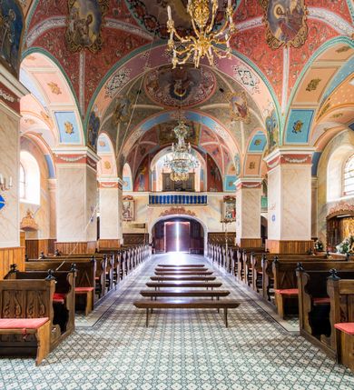 Zdjęcie nr 29: Kościół, zwrócony w kierunku południowo-wschodnim, jest budowlą murowaną z cegły i kamienia, na rzucie podłużnym. Długość bryły wynosi 35, a szerokość 16 metrów. Korpus nawowy jest trójnawowy i czteroprzęsłowy. Stosunkowo szerokie, jednoprzęsłowe, zamknięte półkoliście prezbiterium flankują dwie przyległości, z których jedna jest zakrystią. Na osi kościoła, w przedłużeniu północnego przęsła jest trójkondygnacyjna wieża, ujęta po bokach piętrowymi lokalnościami, lekko wysunięta przed lico fasady. Od zachodu do korpusu przylega kaplica. Nawy przekryte są sklepieniami kolebkowymi wspartymi na filarach o prostokątnym przekroju oraz pilastrach. Przestrzeń prezbiterium od korpusu nawowego oddziela drewniana balustrada. Artykulację ścian na zewnątrz kościoła stanowią osadzone na niewysokim cokole pojedyncze, a w narożach pary lizen wspierających obiegający bryłę fryz, przerwany w partii wieży oraz gzyms. Do wnętrza prowadzą trzy otwory drzwiowe – jeden w elewacji północnej oraz dwa w północnej ścianie kaplicy bocznej. Dwuskrzydłowe drzwi w fasadzie ujęte są profilowanym portalem zamkniętym łukiem odcinkowym zwieńczonym krzyżem. Po bokach wejścia znajduje się para kropielnic. Powyżej otworu drzwiowego usytuowane jest duże okno w kształcie stojącego prostokąta zamkniętego półkoliście, górą ujęte gzymsem. Na wysokości drugiej kondygnacji znajduje się mniejsze okno, zamknięte półkoliście i ujęte prostym obramieniem z kluczem pośrodku oraz parą guttusów pod parapetem. Podobną formę mają cztery okna w ścianach trzeciej kondygnacji wieży, dodatkowo wpisane są one w prostokątne płyciny zamknięte rodzajem łuku kotarowego. W górnej partii wieży znajdują się cztery, okrągłe otwory okienne ujęte prostymi obramieniami zwieńczonymi kluczem. Wieżę wieńczy hełm z osadzoną na cebulastej kopule latarnią zwieńczoną drugą, mniejszą zakończoną krzyżem. Ściany korpusu nawowego i prezbiterium przeprute są prostokątnymi oknami zamkniętymi półkoliście, ujętymi prostym obramieniem z kluczem pośrodku. Okno na zakończeniu prezbiterium jest zamurowane. Okna wypełnione są witrażami, które w prezbiterium zawierają wizerunki Najświętszego Serca Matki Boskiej po prawej i Najświętszego Serca Jezusa po lewej stronie.  Cykl witraży znajduje się także w oknach korpusu, po prawej stronie są to kolejno przedstawienia Matki Boskiej Bolesnej, Boga Ojca, św. Karola Borromeusza i św. Wojciecha, natomiast po lewej stronie – Męża Boleści, Ducha Świętego, św. Jana z Dukli oraz św. Stanisława. Kształt okien korpusu i prezbiterium został powtórzony w kaplicy bocznej, natomiast otwory okienne usytuowane w południowych ścianach przyległości flankujących prezbiterium są w kształcie stojących prostokątów. Korpus nawowy przekryty jest dachem dwuspadowym, wykonanym z blachy. Na wysokości pierwszego przęsła umieszczona jest wieżyczka na sygnaturkę, także obita blachą. Kolorystyka tynków kościoła utrzymana jest w odcieniu jasnożółtym, cokół jest szary natomiast detal architektoniczny jest biały. Plac przykościelny, z wybrukowanymi alejkami i trawnikiem, otoczony jest ogrodzeniem z murowanych słupków i metalowych segmentów.                    