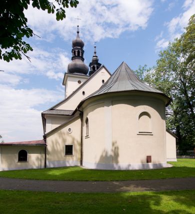 Zdjęcie nr 18: Kościół, zwrócony w kierunku południowo-wschodnim, jest budowlą murowaną z cegły i kamienia, na rzucie podłużnym. Długość bryły wynosi 35, a szerokość 16 metrów. Korpus nawowy jest trójnawowy i czteroprzęsłowy. Stosunkowo szerokie, jednoprzęsłowe, zamknięte półkoliście prezbiterium flankują dwie przyległości, z których jedna jest zakrystią. Na osi kościoła, w przedłużeniu północnego przęsła jest trójkondygnacyjna wieża, ujęta po bokach piętrowymi lokalnościami, lekko wysunięta przed lico fasady. Od zachodu do korpusu przylega kaplica. Nawy przekryte są sklepieniami kolebkowymi wspartymi na filarach o prostokątnym przekroju oraz pilastrach. Przestrzeń prezbiterium od korpusu nawowego oddziela drewniana balustrada. Artykulację ścian na zewnątrz kościoła stanowią osadzone na niewysokim cokole pojedyncze, a w narożach pary lizen wspierających obiegający bryłę fryz, przerwany w partii wieży oraz gzyms. Do wnętrza prowadzą trzy otwory drzwiowe – jeden w elewacji północnej oraz dwa w północnej ścianie kaplicy bocznej. Dwuskrzydłowe drzwi w fasadzie ujęte są profilowanym portalem zamkniętym łukiem odcinkowym zwieńczonym krzyżem. Po bokach wejścia znajduje się para kropielnic. Powyżej otworu drzwiowego usytuowane jest duże okno w kształcie stojącego prostokąta zamkniętego półkoliście, górą ujęte gzymsem. Na wysokości drugiej kondygnacji znajduje się mniejsze okno, zamknięte półkoliście i ujęte prostym obramieniem z kluczem pośrodku oraz parą guttusów pod parapetem. Podobną formę mają cztery okna w ścianach trzeciej kondygnacji wieży, dodatkowo wpisane są one w prostokątne płyciny zamknięte rodzajem łuku kotarowego. W górnej partii wieży znajdują się cztery, okrągłe otwory okienne ujęte prostymi obramieniami zwieńczonymi kluczem. Wieżę wieńczy hełm z osadzoną na cebulastej kopule latarnią zwieńczoną drugą, mniejszą zakończoną krzyżem. Ściany korpusu nawowego i prezbiterium przeprute są prostokątnymi oknami zamkniętymi półkoliście, ujętymi prostym obramieniem z kluczem pośrodku. Okno na zakończeniu prezbiterium jest zamurowane. Okna wypełnione są witrażami, które w prezbiterium zawierają wizerunki Najświętszego Serca Matki Boskiej po prawej i Najświętszego Serca Jezusa po lewej stronie.  Cykl witraży znajduje się także w oknach korpusu, po prawej stronie są to kolejno przedstawienia Matki Boskiej Bolesnej, Boga Ojca, św. Karola Borromeusza i św. Wojciecha, natomiast po lewej stronie – Męża Boleści, Ducha Świętego, św. Jana z Dukli oraz św. Stanisława. Kształt okien korpusu i prezbiterium został powtórzony w kaplicy bocznej, natomiast otwory okienne usytuowane w południowych ścianach przyległości flankujących prezbiterium są w kształcie stojących prostokątów. Korpus nawowy przekryty jest dachem dwuspadowym, wykonanym z blachy. Na wysokości pierwszego przęsła umieszczona jest wieżyczka na sygnaturkę, także obita blachą. Kolorystyka tynków kościoła utrzymana jest w odcieniu jasnożółtym, cokół jest szary natomiast detal architektoniczny jest biały. Plac przykościelny, z wybrukowanymi alejkami i trawnikiem, otoczony jest ogrodzeniem z murowanych słupków i metalowych segmentów.                    