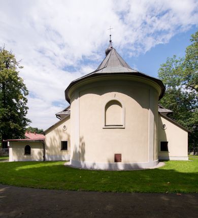Zdjęcie nr 17: Kościół, zwrócony w kierunku południowo-wschodnim, jest budowlą murowaną z cegły i kamienia, na rzucie podłużnym. Długość bryły wynosi 35, a szerokość 16 metrów. Korpus nawowy jest trójnawowy i czteroprzęsłowy. Stosunkowo szerokie, jednoprzęsłowe, zamknięte półkoliście prezbiterium flankują dwie przyległości, z których jedna jest zakrystią. Na osi kościoła, w przedłużeniu północnego przęsła jest trójkondygnacyjna wieża, ujęta po bokach piętrowymi lokalnościami, lekko wysunięta przed lico fasady. Od zachodu do korpusu przylega kaplica. Nawy przekryte są sklepieniami kolebkowymi wspartymi na filarach o prostokątnym przekroju oraz pilastrach. Przestrzeń prezbiterium od korpusu nawowego oddziela drewniana balustrada. Artykulację ścian na zewnątrz kościoła stanowią osadzone na niewysokim cokole pojedyncze, a w narożach pary lizen wspierających obiegający bryłę fryz, przerwany w partii wieży oraz gzyms. Do wnętrza prowadzą trzy otwory drzwiowe – jeden w elewacji północnej oraz dwa w północnej ścianie kaplicy bocznej. Dwuskrzydłowe drzwi w fasadzie ujęte są profilowanym portalem zamkniętym łukiem odcinkowym zwieńczonym krzyżem. Po bokach wejścia znajduje się para kropielnic. Powyżej otworu drzwiowego usytuowane jest duże okno w kształcie stojącego prostokąta zamkniętego półkoliście, górą ujęte gzymsem. Na wysokości drugiej kondygnacji znajduje się mniejsze okno, zamknięte półkoliście i ujęte prostym obramieniem z kluczem pośrodku oraz parą guttusów pod parapetem. Podobną formę mają cztery okna w ścianach trzeciej kondygnacji wieży, dodatkowo wpisane są one w prostokątne płyciny zamknięte rodzajem łuku kotarowego. W górnej partii wieży znajdują się cztery, okrągłe otwory okienne ujęte prostymi obramieniami zwieńczonymi kluczem. Wieżę wieńczy hełm z osadzoną na cebulastej kopule latarnią zwieńczoną drugą, mniejszą zakończoną krzyżem. Ściany korpusu nawowego i prezbiterium przeprute są prostokątnymi oknami zamkniętymi półkoliście, ujętymi prostym obramieniem z kluczem pośrodku. Okno na zakończeniu prezbiterium jest zamurowane. Okna wypełnione są witrażami, które w prezbiterium zawierają wizerunki Najświętszego Serca Matki Boskiej po prawej i Najświętszego Serca Jezusa po lewej stronie.  Cykl witraży znajduje się także w oknach korpusu, po prawej stronie są to kolejno przedstawienia Matki Boskiej Bolesnej, Boga Ojca, św. Karola Borromeusza i św. Wojciecha, natomiast po lewej stronie – Męża Boleści, Ducha Świętego, św. Jana z Dukli oraz św. Stanisława. Kształt okien korpusu i prezbiterium został powtórzony w kaplicy bocznej, natomiast otwory okienne usytuowane w południowych ścianach przyległości flankujących prezbiterium są w kształcie stojących prostokątów. Korpus nawowy przekryty jest dachem dwuspadowym, wykonanym z blachy. Na wysokości pierwszego przęsła umieszczona jest wieżyczka na sygnaturkę, także obita blachą. Kolorystyka tynków kościoła utrzymana jest w odcieniu jasnożółtym, cokół jest szary natomiast detal architektoniczny jest biały. Plac przykościelny, z wybrukowanymi alejkami i trawnikiem, otoczony jest ogrodzeniem z murowanych słupków i metalowych segmentów.                    