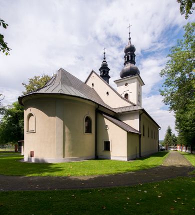 Zdjęcie nr 16: Kościół, zwrócony w kierunku południowo-wschodnim, jest budowlą murowaną z cegły i kamienia, na rzucie podłużnym. Długość bryły wynosi 35, a szerokość 16 metrów. Korpus nawowy jest trójnawowy i czteroprzęsłowy. Stosunkowo szerokie, jednoprzęsłowe, zamknięte półkoliście prezbiterium flankują dwie przyległości, z których jedna jest zakrystią. Na osi kościoła, w przedłużeniu północnego przęsła jest trójkondygnacyjna wieża, ujęta po bokach piętrowymi lokalnościami, lekko wysunięta przed lico fasady. Od zachodu do korpusu przylega kaplica. Nawy przekryte są sklepieniami kolebkowymi wspartymi na filarach o prostokątnym przekroju oraz pilastrach. Przestrzeń prezbiterium od korpusu nawowego oddziela drewniana balustrada. Artykulację ścian na zewnątrz kościoła stanowią osadzone na niewysokim cokole pojedyncze, a w narożach pary lizen wspierających obiegający bryłę fryz, przerwany w partii wieży oraz gzyms. Do wnętrza prowadzą trzy otwory drzwiowe – jeden w elewacji północnej oraz dwa w północnej ścianie kaplicy bocznej. Dwuskrzydłowe drzwi w fasadzie ujęte są profilowanym portalem zamkniętym łukiem odcinkowym zwieńczonym krzyżem. Po bokach wejścia znajduje się para kropielnic. Powyżej otworu drzwiowego usytuowane jest duże okno w kształcie stojącego prostokąta zamkniętego półkoliście, górą ujęte gzymsem. Na wysokości drugiej kondygnacji znajduje się mniejsze okno, zamknięte półkoliście i ujęte prostym obramieniem z kluczem pośrodku oraz parą guttusów pod parapetem. Podobną formę mają cztery okna w ścianach trzeciej kondygnacji wieży, dodatkowo wpisane są one w prostokątne płyciny zamknięte rodzajem łuku kotarowego. W górnej partii wieży znajdują się cztery, okrągłe otwory okienne ujęte prostymi obramieniami zwieńczonymi kluczem. Wieżę wieńczy hełm z osadzoną na cebulastej kopule latarnią zwieńczoną drugą, mniejszą zakończoną krzyżem. Ściany korpusu nawowego i prezbiterium przeprute są prostokątnymi oknami zamkniętymi półkoliście, ujętymi prostym obramieniem z kluczem pośrodku. Okno na zakończeniu prezbiterium jest zamurowane. Okna wypełnione są witrażami, które w prezbiterium zawierają wizerunki Najświętszego Serca Matki Boskiej po prawej i Najświętszego Serca Jezusa po lewej stronie.  Cykl witraży znajduje się także w oknach korpusu, po prawej stronie są to kolejno przedstawienia Matki Boskiej Bolesnej, Boga Ojca, św. Karola Borromeusza i św. Wojciecha, natomiast po lewej stronie – Męża Boleści, Ducha Świętego, św. Jana z Dukli oraz św. Stanisława. Kształt okien korpusu i prezbiterium został powtórzony w kaplicy bocznej, natomiast otwory okienne usytuowane w południowych ścianach przyległości flankujących prezbiterium są w kształcie stojących prostokątów. Korpus nawowy przekryty jest dachem dwuspadowym, wykonanym z blachy. Na wysokości pierwszego przęsła umieszczona jest wieżyczka na sygnaturkę, także obita blachą. Kolorystyka tynków kościoła utrzymana jest w odcieniu jasnożółtym, cokół jest szary natomiast detal architektoniczny jest biały. Plac przykościelny, z wybrukowanymi alejkami i trawnikiem, otoczony jest ogrodzeniem z murowanych słupków i metalowych segmentów.                    
