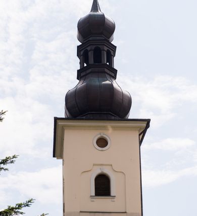 Zdjęcie nr 19: Kościół, zwrócony w kierunku południowo-wschodnim, jest budowlą murowaną z cegły i kamienia, na rzucie podłużnym. Długość bryły wynosi 35, a szerokość 16 metrów. Korpus nawowy jest trójnawowy i czteroprzęsłowy. Stosunkowo szerokie, jednoprzęsłowe, zamknięte półkoliście prezbiterium flankują dwie przyległości, z których jedna jest zakrystią. Na osi kościoła, w przedłużeniu północnego przęsła jest trójkondygnacyjna wieża, ujęta po bokach piętrowymi lokalnościami, lekko wysunięta przed lico fasady. Od zachodu do korpusu przylega kaplica. Nawy przekryte są sklepieniami kolebkowymi wspartymi na filarach o prostokątnym przekroju oraz pilastrach. Przestrzeń prezbiterium od korpusu nawowego oddziela drewniana balustrada. Artykulację ścian na zewnątrz kościoła stanowią osadzone na niewysokim cokole pojedyncze, a w narożach pary lizen wspierających obiegający bryłę fryz, przerwany w partii wieży oraz gzyms. Do wnętrza prowadzą trzy otwory drzwiowe – jeden w elewacji północnej oraz dwa w północnej ścianie kaplicy bocznej. Dwuskrzydłowe drzwi w fasadzie ujęte są profilowanym portalem zamkniętym łukiem odcinkowym zwieńczonym krzyżem. Po bokach wejścia znajduje się para kropielnic. Powyżej otworu drzwiowego usytuowane jest duże okno w kształcie stojącego prostokąta zamkniętego półkoliście, górą ujęte gzymsem. Na wysokości drugiej kondygnacji znajduje się mniejsze okno, zamknięte półkoliście i ujęte prostym obramieniem z kluczem pośrodku oraz parą guttusów pod parapetem. Podobną formę mają cztery okna w ścianach trzeciej kondygnacji wieży, dodatkowo wpisane są one w prostokątne płyciny zamknięte rodzajem łuku kotarowego. W górnej partii wieży znajdują się cztery, okrągłe otwory okienne ujęte prostymi obramieniami zwieńczonymi kluczem. Wieżę wieńczy hełm z osadzoną na cebulastej kopule latarnią zwieńczoną drugą, mniejszą zakończoną krzyżem. Ściany korpusu nawowego i prezbiterium przeprute są prostokątnymi oknami zamkniętymi półkoliście, ujętymi prostym obramieniem z kluczem pośrodku. Okno na zakończeniu prezbiterium jest zamurowane. Okna wypełnione są witrażami, które w prezbiterium zawierają wizerunki Najświętszego Serca Matki Boskiej po prawej i Najświętszego Serca Jezusa po lewej stronie.  Cykl witraży znajduje się także w oknach korpusu, po prawej stronie są to kolejno przedstawienia Matki Boskiej Bolesnej, Boga Ojca, św. Karola Borromeusza i św. Wojciecha, natomiast po lewej stronie – Męża Boleści, Ducha Świętego, św. Jana z Dukli oraz św. Stanisława. Kształt okien korpusu i prezbiterium został powtórzony w kaplicy bocznej, natomiast otwory okienne usytuowane w południowych ścianach przyległości flankujących prezbiterium są w kształcie stojących prostokątów. Korpus nawowy przekryty jest dachem dwuspadowym, wykonanym z blachy. Na wysokości pierwszego przęsła umieszczona jest wieżyczka na sygnaturkę, także obita blachą. Kolorystyka tynków kościoła utrzymana jest w odcieniu jasnożółtym, cokół jest szary natomiast detal architektoniczny jest biały. Plac przykościelny, z wybrukowanymi alejkami i trawnikiem, otoczony jest ogrodzeniem z murowanych słupków i metalowych segmentów.                    