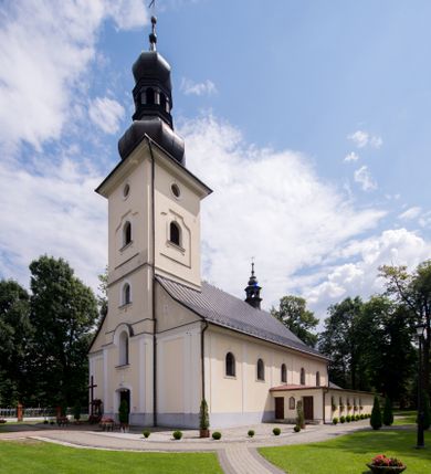Zdjęcie nr 1: Kościół, zwrócony w kierunku południowo-wschodnim, jest budowlą murowaną z cegły i kamienia, na rzucie podłużnym. Długość bryły wynosi 35, a szerokość 16 metrów. Korpus nawowy jest trójnawowy i czteroprzęsłowy. Stosunkowo szerokie, jednoprzęsłowe, zamknięte półkoliście prezbiterium flankują dwie przyległości, z których jedna jest zakrystią. Na osi kościoła, w przedłużeniu północnego przęsła jest trójkondygnacyjna wieża, ujęta po bokach piętrowymi lokalnościami, lekko wysunięta przed lico fasady. Od zachodu do korpusu przylega kaplica. Nawy przekryte są sklepieniami kolebkowymi wspartymi na filarach o prostokątnym przekroju oraz pilastrach. Przestrzeń prezbiterium od korpusu nawowego oddziela drewniana balustrada. Artykulację ścian na zewnątrz kościoła stanowią osadzone na niewysokim cokole pojedyncze, a w narożach pary lizen wspierających obiegający bryłę fryz, przerwany w partii wieży oraz gzyms. Do wnętrza prowadzą trzy otwory drzwiowe – jeden w elewacji północnej oraz dwa w północnej ścianie kaplicy bocznej. Dwuskrzydłowe drzwi w fasadzie ujęte są profilowanym portalem zamkniętym łukiem odcinkowym zwieńczonym krzyżem. Po bokach wejścia znajduje się para kropielnic. Powyżej otworu drzwiowego usytuowane jest duże okno w kształcie stojącego prostokąta zamkniętego półkoliście, górą ujęte gzymsem. Na wysokości drugiej kondygnacji znajduje się mniejsze okno, zamknięte półkoliście i ujęte prostym obramieniem z kluczem pośrodku oraz parą guttusów pod parapetem. Podobną formę mają cztery okna w ścianach trzeciej kondygnacji wieży, dodatkowo wpisane są one w prostokątne płyciny zamknięte rodzajem łuku kotarowego. W górnej partii wieży znajdują się cztery, okrągłe otwory okienne ujęte prostymi obramieniami zwieńczonymi kluczem. Wieżę wieńczy hełm z osadzoną na cebulastej kopule latarnią zwieńczoną drugą, mniejszą zakończoną krzyżem. Ściany korpusu nawowego i prezbiterium przeprute są prostokątnymi oknami zamkniętymi półkoliście, ujętymi prostym obramieniem z kluczem pośrodku. Okno na zakończeniu prezbiterium jest zamurowane. Okna wypełnione są witrażami, które w prezbiterium zawierają wizerunki Najświętszego Serca Matki Boskiej po prawej i Najświętszego Serca Jezusa po lewej stronie.  Cykl witraży znajduje się także w oknach korpusu, po prawej stronie są to kolejno przedstawienia Matki Boskiej Bolesnej, Boga Ojca, św. Karola Borromeusza i św. Wojciecha, natomiast po lewej stronie – Męża Boleści, Ducha Świętego, św. Jana z Dukli oraz św. Stanisława. Kształt okien korpusu i prezbiterium został powtórzony w kaplicy bocznej, natomiast otwory okienne usytuowane w południowych ścianach przyległości flankujących prezbiterium są w kształcie stojących prostokątów. Korpus nawowy przekryty jest dachem dwuspadowym, wykonanym z blachy. Na wysokości pierwszego przęsła umieszczona jest wieżyczka na sygnaturkę, także obita blachą. Kolorystyka tynków kościoła utrzymana jest w odcieniu jasnożółtym, cokół jest szary natomiast detal architektoniczny jest biały. Plac przykościelny, z wybrukowanymi alejkami i trawnikiem, otoczony jest ogrodzeniem z murowanych słupków i metalowych segmentów.                    