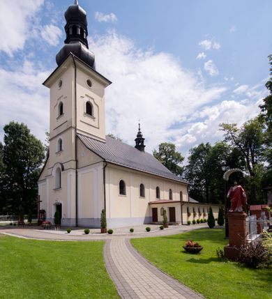 Zdjęcie nr 3: Kościół, zwrócony w kierunku południowo-wschodnim, jest budowlą murowaną z cegły i kamienia, na rzucie podłużnym. Długość bryły wynosi 35, a szerokość 16 metrów. Korpus nawowy jest trójnawowy i czteroprzęsłowy. Stosunkowo szerokie, jednoprzęsłowe, zamknięte półkoliście prezbiterium flankują dwie przyległości, z których jedna jest zakrystią. Na osi kościoła, w przedłużeniu północnego przęsła jest trójkondygnacyjna wieża, ujęta po bokach piętrowymi lokalnościami, lekko wysunięta przed lico fasady. Od zachodu do korpusu przylega kaplica. Nawy przekryte są sklepieniami kolebkowymi wspartymi na filarach o prostokątnym przekroju oraz pilastrach. Przestrzeń prezbiterium od korpusu nawowego oddziela drewniana balustrada. Artykulację ścian na zewnątrz kościoła stanowią osadzone na niewysokim cokole pojedyncze, a w narożach pary lizen wspierających obiegający bryłę fryz, przerwany w partii wieży oraz gzyms. Do wnętrza prowadzą trzy otwory drzwiowe – jeden w elewacji północnej oraz dwa w północnej ścianie kaplicy bocznej. Dwuskrzydłowe drzwi w fasadzie ujęte są profilowanym portalem zamkniętym łukiem odcinkowym zwieńczonym krzyżem. Po bokach wejścia znajduje się para kropielnic. Powyżej otworu drzwiowego usytuowane jest duże okno w kształcie stojącego prostokąta zamkniętego półkoliście, górą ujęte gzymsem. Na wysokości drugiej kondygnacji znajduje się mniejsze okno, zamknięte półkoliście i ujęte prostym obramieniem z kluczem pośrodku oraz parą guttusów pod parapetem. Podobną formę mają cztery okna w ścianach trzeciej kondygnacji wieży, dodatkowo wpisane są one w prostokątne płyciny zamknięte rodzajem łuku kotarowego. W górnej partii wieży znajdują się cztery, okrągłe otwory okienne ujęte prostymi obramieniami zwieńczonymi kluczem. Wieżę wieńczy hełm z osadzoną na cebulastej kopule latarnią zwieńczoną drugą, mniejszą zakończoną krzyżem. Ściany korpusu nawowego i prezbiterium przeprute są prostokątnymi oknami zamkniętymi półkoliście, ujętymi prostym obramieniem z kluczem pośrodku. Okno na zakończeniu prezbiterium jest zamurowane. Okna wypełnione są witrażami, które w prezbiterium zawierają wizerunki Najświętszego Serca Matki Boskiej po prawej i Najświętszego Serca Jezusa po lewej stronie.  Cykl witraży znajduje się także w oknach korpusu, po prawej stronie są to kolejno przedstawienia Matki Boskiej Bolesnej, Boga Ojca, św. Karola Borromeusza i św. Wojciecha, natomiast po lewej stronie – Męża Boleści, Ducha Świętego, św. Jana z Dukli oraz św. Stanisława. Kształt okien korpusu i prezbiterium został powtórzony w kaplicy bocznej, natomiast otwory okienne usytuowane w południowych ścianach przyległości flankujących prezbiterium są w kształcie stojących prostokątów. Korpus nawowy przekryty jest dachem dwuspadowym, wykonanym z blachy. Na wysokości pierwszego przęsła umieszczona jest wieżyczka na sygnaturkę, także obita blachą. Kolorystyka tynków kościoła utrzymana jest w odcieniu jasnożółtym, cokół jest szary natomiast detal architektoniczny jest biały. Plac przykościelny, z wybrukowanymi alejkami i trawnikiem, otoczony jest ogrodzeniem z murowanych słupków i metalowych segmentów.                    