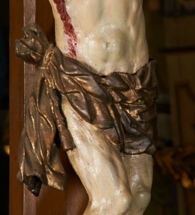 Zdjęcie nr 16: Rzeźba przybita jest trzema gwoździami do prostego krzyża umieszczonego na belce tęczowej. Chrystus ukazany został w typie Cristo morte (umarłego), w lekkim zwisie ciała, o szeroko rozłożonych ramionach przyjmujących kształt delikatnego łuku. Jego głowa opada bezwładnie na prawy bark, nogi ma ugięte w kolanach, skierowane lekko w lewo, w efekcie całe ciało wygina się w pionie w niezbyt wydatny łuk. Stopy skrzyżowane w układzie prawa na lewą. Twarz ma podłużną, o prostym, wąskim nosie, dużych, zamkniętych oczach i niewielkich ustach, okoloną brodą skręconą w dwa pukle oraz pasmami kręconych włosów opadających na ramiona. Na głowie ma koronę cierniową. Jego ciało jest szczupłe, smukłe, o miękko rzeźbionej muskulaturze, silnie podkreślonej w partiach klatki piersiowej, nóg i ramion, z zaznaczonymi śladami męki w postaci broczących rzeźbionymi kroplami krwi ran. Perizonium ma krótkie, ściśle przylegające do ciała, obficie fałdowane zawiązane na prawym biodrze. Polichromia naturalistyczna, perizonium pozłacane. Na pionowej belce krzyża tabliczka z napisem „I.N. / R.I.”. 