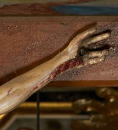 Zdjęcie nr 6: Rzeźba przybita jest trzema gwoździami do prostego krzyża umieszczonego na belce tęczowej. Chrystus ukazany został w typie Cristo morte (umarłego), w lekkim zwisie ciała, o szeroko rozłożonych ramionach przyjmujących kształt delikatnego łuku. Jego głowa opada bezwładnie na prawy bark, nogi ma ugięte w kolanach, skierowane lekko w lewo, w efekcie całe ciało wygina się w pionie w niezbyt wydatny łuk. Stopy skrzyżowane w układzie prawa na lewą. Twarz ma podłużną, o prostym, wąskim nosie, dużych, zamkniętych oczach i niewielkich ustach, okoloną brodą skręconą w dwa pukle oraz pasmami kręconych włosów opadających na ramiona. Na głowie ma koronę cierniową. Jego ciało jest szczupłe, smukłe, o miękko rzeźbionej muskulaturze, silnie podkreślonej w partiach klatki piersiowej, nóg i ramion, z zaznaczonymi śladami męki w postaci broczących rzeźbionymi kroplami krwi ran. Perizonium ma krótkie, ściśle przylegające do ciała, obficie fałdowane zawiązane na prawym biodrze. Polichromia naturalistyczna, perizonium pozłacane. Na pionowej belce krzyża tabliczka z napisem „I.N. / R.I.”. 