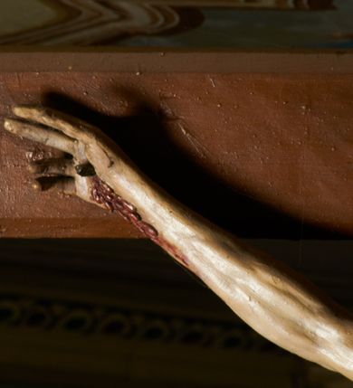 Zdjęcie nr 5: Rzeźba przybita jest trzema gwoździami do prostego krzyża umieszczonego na belce tęczowej. Chrystus ukazany został w typie Cristo morte (umarłego), w lekkim zwisie ciała, o szeroko rozłożonych ramionach przyjmujących kształt delikatnego łuku. Jego głowa opada bezwładnie na prawy bark, nogi ma ugięte w kolanach, skierowane lekko w lewo, w efekcie całe ciało wygina się w pionie w niezbyt wydatny łuk. Stopy skrzyżowane w układzie prawa na lewą. Twarz ma podłużną, o prostym, wąskim nosie, dużych, zamkniętych oczach i niewielkich ustach, okoloną brodą skręconą w dwa pukle oraz pasmami kręconych włosów opadających na ramiona. Na głowie ma koronę cierniową. Jego ciało jest szczupłe, smukłe, o miękko rzeźbionej muskulaturze, silnie podkreślonej w partiach klatki piersiowej, nóg i ramion, z zaznaczonymi śladami męki w postaci broczących rzeźbionymi kroplami krwi ran. Perizonium ma krótkie, ściśle przylegające do ciała, obficie fałdowane zawiązane na prawym biodrze. Polichromia naturalistyczna, perizonium pozłacane. Na pionowej belce krzyża tabliczka z napisem „I.N. / R.I.”. 