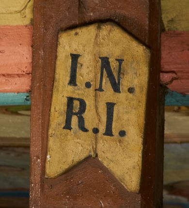 Zdjęcie nr 7: Rzeźba przybita jest trzema gwoździami do prostego krzyża umieszczonego na belce tęczowej. Chrystus ukazany został w typie Cristo morte (umarłego), w lekkim zwisie ciała, o szeroko rozłożonych ramionach przyjmujących kształt delikatnego łuku. Jego głowa opada bezwładnie na prawy bark, nogi ma ugięte w kolanach, skierowane lekko w lewo, w efekcie całe ciało wygina się w pionie w niezbyt wydatny łuk. Stopy skrzyżowane w układzie prawa na lewą. Twarz ma podłużną, o prostym, wąskim nosie, dużych, zamkniętych oczach i niewielkich ustach, okoloną brodą skręconą w dwa pukle oraz pasmami kręconych włosów opadających na ramiona. Na głowie ma koronę cierniową. Jego ciało jest szczupłe, smukłe, o miękko rzeźbionej muskulaturze, silnie podkreślonej w partiach klatki piersiowej, nóg i ramion, z zaznaczonymi śladami męki w postaci broczących rzeźbionymi kroplami krwi ran. Perizonium ma krótkie, ściśle przylegające do ciała, obficie fałdowane zawiązane na prawym biodrze. Polichromia naturalistyczna, perizonium pozłacane. Na pionowej belce krzyża tabliczka z napisem „I.N. / R.I.”. 