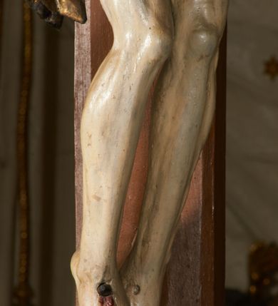 Zdjęcie nr 3: Rzeźba przybita jest trzema gwoździami do prostego krzyża umieszczonego na belce tęczowej. Chrystus ukazany został w typie Cristo morte (umarłego), w lekkim zwisie ciała, o szeroko rozłożonych ramionach przyjmujących kształt delikatnego łuku. Jego głowa opada bezwładnie na prawy bark, nogi ma ugięte w kolanach, skierowane lekko w lewo, w efekcie całe ciało wygina się w pionie w niezbyt wydatny łuk. Stopy skrzyżowane w układzie prawa na lewą. Twarz ma podłużną, o prostym, wąskim nosie, dużych, zamkniętych oczach i niewielkich ustach, okoloną brodą skręconą w dwa pukle oraz pasmami kręconych włosów opadających na ramiona. Na głowie ma koronę cierniową. Jego ciało jest szczupłe, smukłe, o miękko rzeźbionej muskulaturze, silnie podkreślonej w partiach klatki piersiowej, nóg i ramion, z zaznaczonymi śladami męki w postaci broczących rzeźbionymi kroplami krwi ran. Perizonium ma krótkie, ściśle przylegające do ciała, obficie fałdowane zawiązane na prawym biodrze. Polichromia naturalistyczna, perizonium pozłacane. Na pionowej belce krzyża tabliczka z napisem „I.N. / R.I.”. 