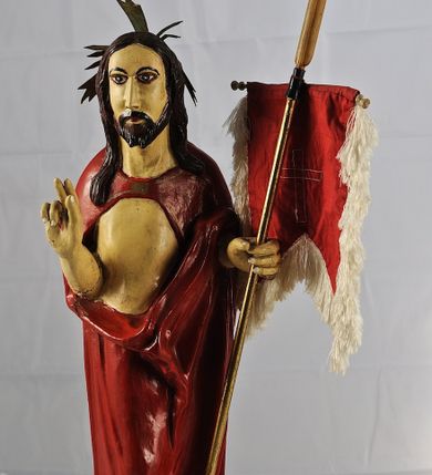 Zdjęcie nr 1: Figura pełnoplastyczna ustawiona na podstawie na planie kwadratu oraz na półkuli. Chrystus stoi frontalnie, w kontrapoście, w lewej ręce trzyma drzewce chorągwi zakończone krzyżem, prawą unosi w geście błogosławieństwa. Jego twarz jest pociągła, o długim, prostym nosie, migdałowatych oczach i niewielkich ustach, okolona krótką brodą i długimi włosami opadającymi na ramiona i plecy. Z tyłu  jego głowy jest dosztukowany nimb promienisty. Chrystus ubrany jest w czerwony płaszcz odsłaniający tors, zapięty na piersi, mocno pofałdowany na wysokości bioder, otaczający postać i przerzucony przez lewe przedramię. Polichromia naturalistyczna, drzewce chorągwi pozłacane.