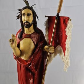 Zdjęcie nr 1: Figura pełnoplastyczna ustawiona na podstawie na planie kwadratu oraz na półkuli. Chrystus stoi frontalnie, w kontrapoście, w lewej ręce trzyma drzewce chorągwi zakończone krzyżem, prawą unosi w geście błogosławieństwa. Jego twarz jest pociągła, o długim, prostym nosie, migdałowatych oczach i niewielkich ustach, okolona krótką brodą i długimi włosami opadającymi na ramiona i plecy. Z tyłu  jego głowy jest dosztukowany nimb promienisty. Chrystus ubrany jest w czerwony płaszcz odsłaniający tors, zapięty na piersi, mocno pofałdowany na wysokości bioder, otaczający postać i przerzucony przez lewe przedramię. Polichromia naturalistyczna, drzewce chorągwi pozłacane.