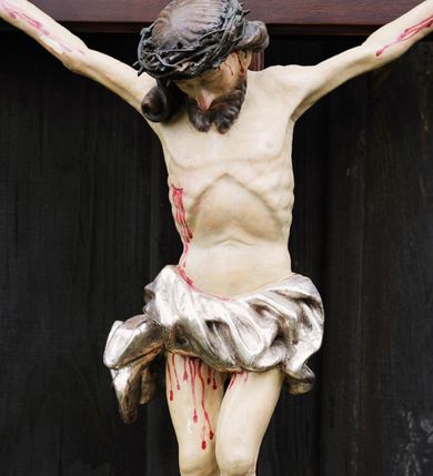 Zdjęcie nr 2: Do krzyża o prostych ramionach przybita trzema gwoździami figura w typie Cristo morte. Ciało Chrystusa jest w lekkim zwisie, o szeroko rozłożonych ramionach, jego głowa opada bezwładnie na prawy bark, lewa noga ugięta jest w kolanie, prawa wyprostowana, stopy skrzyżowane w układzie lewa na prawą. Twarz ma pociągłą, o dużym nosie, zamkniętych oczach i lekko rozchylonych ustach, okoloną krótką, rozdwajającą się brodą oraz długimi włosami opadającymi na prawy bark, skręconymi w jeden, duży pukiel. Na głowie ma koronę cierniową. Jego ciało jest szczupłe, o silnie uwypuklonym kośćcu klatki piersiowej z guzowato rzeźbionymi żebrami i zapadłą płaszczyzną brzucha. Perizonium krótkie, w formie skręconej tkaniny ze zwisem na prawym boku. Na zakończeniu pionowej belki krzyża banderola z napisem „IN/RI”. Polichromia naturalistyczna w partii karnacji, o bladym odcieniu, z zaznaczonymi malowaną krwią ranami, włosy i broda brązowe, perizonium srebrzone. 
