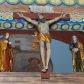 Zdjęcie nr 1: Grupa na tęczy składa się z na wpół ludowo rzeźbionego centralnie krucyfiksu z martwym Chrystusem, po bokach którego stoi pełnorzeźbiona Matka Boska Bolesna i św. Jan Ewangelista. Zbawiciel do krzyża został przymocowany trzema gwoździami. Jezus został ukazany jako martwy z zamkniętymi oczami i głową opadającą na piersi. Jego postać jest wysmukła z nienaturalnie potraktowaną muskulaturą korpusu. Ciało jest wychudzone o zapadłej klatce piersiowej z podkreśloną linią żeber i mostkiem. Z prawej strony widoczny jest przebity bok. Nieznacznie rozchylone nogi są sztywne w kolanach. Prawa stopa założona jest na lewą. Pociągła twarz Chrystusa została miękko opracowana bez szczególnej dbałości o szczegóły anatomiczne. Chrystus ma zamknięte oczy, prosty nos oraz lekko otwarte usta otoczone ciemnobrązowym zarostem, przechodzącym w brodę nieznacznie rozdwojoną na końcu. Jego ciemnobrązowe włosy z lekkim puklowaniem opadają pasmem z prawej strony na ramię, a z lewej na kark, odsłaniając wydatną małżowinę lewego ucha. Chrystus ma na głowie srebrzoną laserunkowo, cierniową koronę, spod której na czoło spływają krople krwi. Krew widoczna jest również na jego rękach, torsie i nogach. Charakterystycznie rzeźbione są nieproporcjonalnie duże dłonie o dwóch zgiętych palcach. Biodra Zbawiciela przepasane są złoconym, krótkim perizonium w formie chusty zawiązanej na duży węzeł z festonem opadającym wzdłuż prawego boku. Ponad głową Chrystusa zawieszony jest titulus w formie tabliczki o faliście wycinanych brzegach ze złotym napisem: „INRI”. 
Stojąca na lekkim wzgórku Matka Boska Bolesna ukazana została w ujęciu trzy czwarte w lewo w nieznacznym kontrapoście. Zgięte w łokciach ręce o nieproporcjonalnie dużych dłoniach ma skrzyżowane na piersi. Maria ma podłużną twarz pozbawioną cech szczególnych. Jej głowę osłania złocona chusta opadająca na ramiona, spod której widoczne są pasma brązowych włosów. Ubrana jest w długą, ciemnoochrową suknię, malowaną laserunkiem, przepasaną w tali oraz płaszcz narzucony na ramiona. Spod sukni widać czubki stóp. 
Święty Jan Ewangelista został zwrócony trzy czwarte w prawo w lekkim kontrapoście. Stojąc na niewielkim wzgórku, trzyma na wysokości brzucha splecione nieproporcjonalnie duże dłonie. Święty ma pociągłą twarz okoloną półdługimi, mocno kręconymi włosami, których pasma z lewej strony odsłaniają wydatną małżowinę uszną. Bardzo mocno zaakcentowano jego krtań. Apostoł ubrany jest w długą tunikę z charakterystycznym kołnierzykiem, malowaną laserunkiem na ciemnooliwkowo oraz złocony płaszcz narzucony na lewe ramię, którego połę zdaje się przyciskać do pasa prawą ręką. Spod tuniki widoczne są czubki stóp. 
Na zachowanym fragmencie oryginalnej belki tęczowej widnieje czerwona inskrypcja: „[...]IT ET IN HONOREN SANCTE MARIE / MAGDALE”. 
