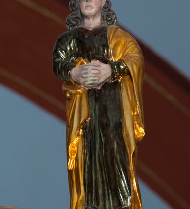 Zdjęcie nr 6: Grupa na tęczy składa się z na wpół ludowo rzeźbionego centralnie krucyfiksu z martwym Chrystusem, po bokach którego stoi pełnorzeźbiona Matka Boska Bolesna i św. Jan Ewangelista. Zbawiciel do krzyża został przymocowany trzema gwoździami. Jezus został ukazany jako martwy z zamkniętymi oczami i głową opadającą na piersi. Jego postać jest wysmukła z nienaturalnie potraktowaną muskulaturą korpusu. Ciało jest wychudzone o zapadłej klatce piersiowej z podkreśloną linią żeber i mostkiem. Z prawej strony widoczny jest przebity bok. Nieznacznie rozchylone nogi są sztywne w kolanach. Prawa stopa założona jest na lewą. Pociągła twarz Chrystusa została miękko opracowana bez szczególnej dbałości o szczegóły anatomiczne. Chrystus ma zamknięte oczy, prosty nos oraz lekko otwarte usta otoczone ciemnobrązowym zarostem, przechodzącym w brodę nieznacznie rozdwojoną na końcu. Jego ciemnobrązowe włosy z lekkim puklowaniem opadają pasmem z prawej strony na ramię, a z lewej na kark, odsłaniając wydatną małżowinę lewego ucha. Chrystus ma na głowie srebrzoną laserunkowo, cierniową koronę, spod której na czoło spływają krople krwi. Krew widoczna jest również na jego rękach, torsie i nogach. Charakterystycznie rzeźbione są nieproporcjonalnie duże dłonie o dwóch zgiętych palcach. Biodra Zbawiciela przepasane są złoconym, krótkim perizonium w formie chusty zawiązanej na duży węzeł z festonem opadającym wzdłuż prawego boku. Ponad głową Chrystusa zawieszony jest titulus w formie tabliczki o faliście wycinanych brzegach ze złotym napisem: „INRI”. 
Stojąca na lekkim wzgórku Matka Boska Bolesna ukazana została w ujęciu trzy czwarte w lewo w nieznacznym kontrapoście. Zgięte w łokciach ręce o nieproporcjonalnie dużych dłoniach ma skrzyżowane na piersi. Maria ma podłużną twarz pozbawioną cech szczególnych. Jej głowę osłania złocona chusta opadająca na ramiona, spod której widoczne są pasma brązowych włosów. Ubrana jest w długą, ciemnoochrową suknię, malowaną laserunkiem, przepasaną w tali oraz płaszcz narzucony na ramiona. Spod sukni widać czubki stóp. 
Święty Jan Ewangelista został zwrócony trzy czwarte w prawo w lekkim kontrapoście. Stojąc na niewielkim wzgórku, trzyma na wysokości brzucha splecione nieproporcjonalnie duże dłonie. Święty ma pociągłą twarz okoloną półdługimi, mocno kręconymi włosami, których pasma z lewej strony odsłaniają wydatną małżowinę uszną. Bardzo mocno zaakcentowano jego krtań. Apostoł ubrany jest w długą tunikę z charakterystycznym kołnierzykiem, malowaną laserunkiem na ciemnooliwkowo oraz złocony płaszcz narzucony na lewe ramię, którego połę zdaje się przyciskać do pasa prawą ręką. Spod tuniki widoczne są czubki stóp. 
Na zachowanym fragmencie oryginalnej belki tęczowej widnieje czerwona inskrypcja: „[...]IT ET IN HONOREN SANCTE MARIE / MAGDALE”. 
