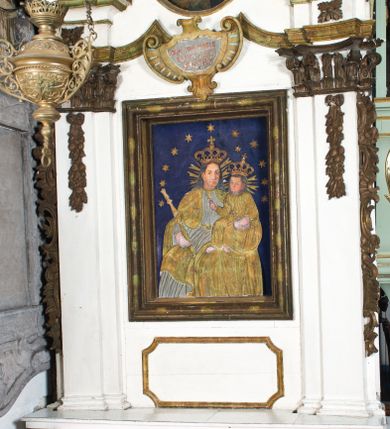 Zdjęcie nr 1: Przyścienne retabulum wznosi się nad sarkofagowym stipesie z drewnianą mensą z kamiennym portatylem, ustawowym na cokole, wspartym na drewnianym podeście. Stipes zwęża się ku dołowi. Od frontu zdobi go fantazyjne obramienie utworzone z profilowanej listwy przechodzącej na środku w płaskorzeźbiony ornament muszlowy. Ponad ołtarzem wznosi się jednoosiowe i jednokondygnacyjne retabulum ze zwieńczeniem ustawione na wysokim cokole. Nastawę artykułuje para zdwojonych pilastrów o korynckich głowicach z trzonami dekorowanymi zawieszonymi na wstęgach festonach owocowo-kwiatowych. Pilastry dźwigają imposty o wyłamanym wklęśle gzymsie, oraz przerwany półkolisty przyczółek. Imposty połączone zostały architrawem nad polem głównym, przyjmującym kształt odwróconego łuku odcinkowego, dekorowanego muszlowym kartuszem z napisem: „ORA PRO NOBIS / SANCTA DEI / GENITRIX”. W polu środkowym umieszczono obraz Matki Boskiej z Dzieciątkiem w formie stojącego prostokąta ujęty profilowaną ramą. Poniżej obrazu znalazła się ramka w formie leżącego prostokąta o wklęsłych bokach. Zwieńczenie uzyskało formę stojącego prostokąta o wklęsłych bokach zamknięty całującymi się wolutami i muszlą. W polu zwieńczenia umieszczono owalny obraz św. Antoniego Padewskiego, ujęty profilowaną ramą. Ponad nim znajdują się dekoracyjne, profilowane listewki układające się w fantazyjne kształty. Po bokach retabulum usytuowano zredukowane uszaki w formie wąskich, ażurowych wici roślinnych. Strukturę nastawy polichromowano na biało, ornamentyka i profile pierwotnie były złocone.