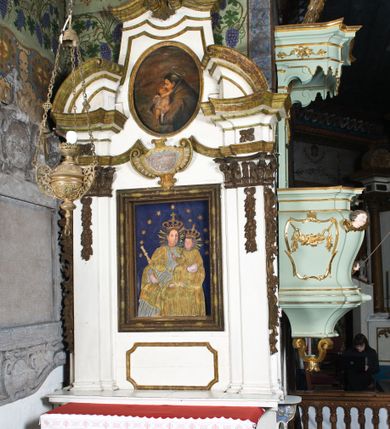 Zdjęcie nr 5: Przyścienne retabulum wznosi się nad sarkofagowym stipesie z drewnianą mensą z kamiennym portatylem, ustawowym na cokole, wspartym na drewnianym podeście. Stipes zwęża się ku dołowi. Od frontu zdobi go fantazyjne obramienie utworzone z profilowanej listwy przechodzącej na środku w płaskorzeźbiony ornament muszlowy. Ponad ołtarzem wznosi się jednoosiowe i jednokondygnacyjne retabulum ze zwieńczeniem ustawione na wysokim cokole. Nastawę artykułuje para zdwojonych pilastrów o korynckich głowicach z trzonami dekorowanymi zawieszonymi na wstęgach festonach owocowo-kwiatowych. Pilastry dźwigają imposty o wyłamanym wklęśle gzymsie, oraz przerwany półkolisty przyczółek. Imposty połączone zostały architrawem nad polem głównym, przyjmującym kształt odwróconego łuku odcinkowego, dekorowanego muszlowym kartuszem z napisem: „ORA PRO NOBIS / SANCTA DEI / GENITRIX”. W polu środkowym umieszczono obraz Matki Boskiej z Dzieciątkiem w formie stojącego prostokąta ujęty profilowaną ramą. Poniżej obrazu znalazła się ramka w formie leżącego prostokąta o wklęsłych bokach. Zwieńczenie uzyskało formę stojącego prostokąta o wklęsłych bokach zamknięty całującymi się wolutami i muszlą. W polu zwieńczenia umieszczono owalny obraz św. Antoniego Padewskiego, ujęty profilowaną ramą. Ponad nim znajdują się dekoracyjne, profilowane listewki układające się w fantazyjne kształty. Po bokach retabulum usytuowano zredukowane uszaki w formie wąskich, ażurowych wici roślinnych. Strukturę nastawy polichromowano na biało, ornamentyka i profile pierwotnie były złocone.