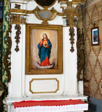 Zdjęcie nr 6: Przyścienne retabulum wznosi się nad sarkofagowym stipesie z drewnianą mensą z kamiennym portatylem, ustawowym na cokole, wspartym na drewnianym podeście. Stipes zwęża się ku dołowi. Od frontu zdobi go fantazyjne obramienie utworzone z profilowanej listwy przechodzącej na środku w płaskorzeźbiony ornament muszlowy. Ponad ołtarzem wznosi się jednoosiowe i jednokondygnacyjne retabulum ze zwieńczeniem ustawione na wysokim cokole. Nastawę artykułuje para zdwojonych pilastrów o korynckich głowicach z trzonami dekorowanymi zawieszonymi na wstęgach festonach owocowo-kwiatowych. Pilastry dźwigają imposty o wyłamanym wklęśle gzymsie, oraz przerwany półkolisty przyczółek. Imposty połączone zostały architrawem nad polem głównym, przyjmującym kształt odwróconego łuku odcinkowego, dekorowanego muszlowym kartuszem. W polu środkowym umieszczono obraz Najświętszego Serca Pana Jezusa w formie stojącego prostokąta ujęty profilowaną ramą. Poniżej obrazu znalazła się ramka w formie leżącego prostokąta o wklęsłych bokach. Zwieńczenie uzyskało formę stojącego prostokąta o wklęsłych bokach zamknięty całującymi się wolutami i muszlą. W polu zwieńczenia umieszczono owalny obraz św. Józefa, ujęty profilowaną ramą. Ponad nim znajdują się dekoracyjne, profilowane listewki układające się w fantazyjne kształty. Po bokach retabulum usytuowano zredukowane uszaki w formie wąskich, ażurowych wici roślinnych. Strukturę nastawy polichromowano na biało, ornamentyka i profile pierwotnie były złocone.