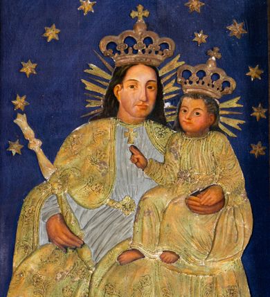 Zdjęcie nr 1: Obraz uzyskał formę stojącego prostokąta. W centrum kompozycji na ciemnoniebieskim tle utworzonym z tkaniny ukazano frontalnie w dwóch trzecich Madonnę z Dzieciątkiem. Obie postacie przykrywa płaskorzeźbiona, drewniana sukienka wotywna z koronami i berłem. Matka Boska na lewym ramieniu trzyma Dzieciątko, a w prawej ręce berło. Głowa Madonny ujęta została w trzech czwartych w lewo. Maria ma pociągłą twarz, wysokie czoło, prosty, długi nos i wydatne usta oraz ciemne oczy o spojrzeniu skierowanym na widza. Jej głowę otaczają ciemne włosy spływające na ramiona. Ubrana jest w luźną, srebrzoną suknię przepasaną w pasie i narzucony na nią złocony płaszcz. Pod szyją ma zawieszony złocony krzyżyk. Dzieciątko Jezus ukazane zostało w trzech czwartych w prawo. Prawą rękę ma uniesioną w geście błogosławieństwa, lewą zaś wspiera na lewej dłoni matki. Jezus ma owalną twarz, wydatny nos i usta oraz szeroko otwarte ciemne oczy o spojrzeniu skierowanym na widza. Na głowach obu postaci otoczonych promieniami widnieją korony zamknięte oraz wieniec z gwiazd.