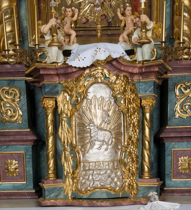 Zdjęcie nr 43: Kamienny ołtarz w jawiszowickim kościele uzyskał kształt prostopadłościanu. Otacza go drewniana obudowa podtrzymująca drewnianą mensę z portatylem. Jego przód zdobi drewniane antepedium ujęte profilowaną ramą z centralnym medalionem z monogramem Marii, otoczonym przez ornament roślinny. Ponad ołtarzem rozpościera się dwukondygnacyjna, architektoniczna nastawa ołtarzowa, flankowana przez dwie bramki. Struktura ołtarza dekorowana jest ciemnozieloną marmoryzacją. Pierwsza kondygnacja retabulum uzyskała trójosiowe założenie wsparte na dwustrefowym cokole, podzielonym płycinami z dekoracją akantową. Artykułują ją dwie pary kolumn o skręconych trzonach i kapitelach kompozytowych. Złocone w całości kolumny podtrzymują belkowanie o wysuniętym gzymsie, wyłamane na ich osi oraz przerwany trójkątny przyczółek. Pole środkowe nastawy wypełnia w całości nisza ujęta profilowaną, złoconą ramą w formie stojącego prostokąta zamkniętego trzema bokami z ośmioboku. W jej wnętrzu znajduje się obraz Matki Boskiej z Dzieciątkiem w typie Matki Boskiej Śnieżnej, zdobiony drewnianą złoconą i srebrzoną sukienką wotywną oraz koronami, a także dwie zasuwy z przedstawieniem św. Marcina, biskupa oraz bł. Salomei. Niszę środkową flankują znajdujące się pomiędzy kolumnami wąskie płyciny zwieńczone konchami. Na ich tle ustawiono figury św. Piotra i św. Pawła. Ponad nimi widoczne są na belkowaniu płaskorzeźbione i złocone girlandy kwiatowe oraz rozety. Na przerwanym przyczółku umieszczono dwie figury siedzących aniołów. Na mensie ołtarza centralnie ustawiono prostopadłościenne tabernakulum w drewnianej obudowie ujęte dwiema kolumienkami kompozytowymi o skręconych trzonach podtrzymujących belkowanie, do którego przymocowano świeczniki na sakramentki. Umieszczony na jego szczycie prosty tron eucharystyczny bez zaplecka flankują dwie figury uskrzydlonych aniołków. Drugą, jednoosiową kondygnację nastawy ujmuje także para złoconych kolumn o skręconych trzonach i kapitelach kompozytowych, ustawionych na cokołach, dźwigających imposty. Pomiędzy kolumnami nad polem z obrazem Wniebowzięcia Matki Boskiej widoczny jest wysunięty fragment gzymsu. Obraz ujęty został złoconą i profilowaną ramą w formie kwadratu o ściętych narożach. Po bokach obrazu na płycinie rozmieszczono złocone dekoracje akantowe. W zwieńczeniu na belkowaniu usytuowano dwa putta flankujące rzeźbę apokaliptycznego baranka leżącego na księdze. Obie kondygnacje ujmują uszaki z akantu suchego. Po bokach nastawy usytuowano dwie bramki flankowane pilastrami. Ich zwężające się ku dołowi trzony podtrzymują nadwieszony łuk półkolisty. Całość zamyka gzyms z centralnie usytuowanym cokołem, na którym stoją figury św. Stanisława i św. Wojciecha. Po ich bokach figur przy ścianach ustawiono rzeźbione i złocone wazony z kwiatami. 