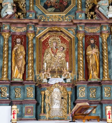 Zdjęcie nr 34: Kamienny ołtarz w jawiszowickim kościele uzyskał kształt prostopadłościanu. Otacza go drewniana obudowa podtrzymująca drewnianą mensę z portatylem. Jego przód zdobi drewniane antepedium ujęte profilowaną ramą z centralnym medalionem z monogramem Marii, otoczonym przez ornament roślinny. Ponad ołtarzem rozpościera się dwukondygnacyjna, architektoniczna nastawa ołtarzowa, flankowana przez dwie bramki. Struktura ołtarza dekorowana jest ciemnozieloną marmoryzacją. Pierwsza kondygnacja retabulum uzyskała trójosiowe założenie wsparte na dwustrefowym cokole, podzielonym płycinami z dekoracją akantową. Artykułują ją dwie pary kolumn o skręconych trzonach i kapitelach kompozytowych. Złocone w całości kolumny podtrzymują belkowanie o wysuniętym gzymsie, wyłamane na ich osi oraz przerwany trójkątny przyczółek. Pole środkowe nastawy wypełnia w całości nisza ujęta profilowaną, złoconą ramą w formie stojącego prostokąta zamkniętego trzema bokami z ośmioboku. W jej wnętrzu znajduje się obraz Matki Boskiej z Dzieciątkiem w typie Matki Boskiej Śnieżnej, zdobiony drewnianą złoconą i srebrzoną sukienką wotywną oraz koronami, a także dwie zasuwy z przedstawieniem św. Marcina, biskupa oraz bł. Salomei. Niszę środkową flankują znajdujące się pomiędzy kolumnami wąskie płyciny zwieńczone konchami. Na ich tle ustawiono figury św. Piotra i św. Pawła. Ponad nimi widoczne są na belkowaniu płaskorzeźbione i złocone girlandy kwiatowe oraz rozety. Na przerwanym przyczółku umieszczono dwie figury siedzących aniołów. Na mensie ołtarza centralnie ustawiono prostopadłościenne tabernakulum w drewnianej obudowie ujęte dwiema kolumienkami kompozytowymi o skręconych trzonach podtrzymujących belkowanie, do którego przymocowano świeczniki na sakramentki. Umieszczony na jego szczycie prosty tron eucharystyczny bez zaplecka flankują dwie figury uskrzydlonych aniołków. Drugą, jednoosiową kondygnację nastawy ujmuje także para złoconych kolumn o skręconych trzonach i kapitelach kompozytowych, ustawionych na cokołach, dźwigających imposty. Pomiędzy kolumnami nad polem z obrazem Wniebowzięcia Matki Boskiej widoczny jest wysunięty fragment gzymsu. Obraz ujęty został złoconą i profilowaną ramą w formie kwadratu o ściętych narożach. Po bokach obrazu na płycinie rozmieszczono złocone dekoracje akantowe. W zwieńczeniu na belkowaniu usytuowano dwa putta flankujące rzeźbę apokaliptycznego baranka leżącego na księdze. Obie kondygnacje ujmują uszaki z akantu suchego. Po bokach nastawy usytuowano dwie bramki flankowane pilastrami. Ich zwężające się ku dołowi trzony podtrzymują nadwieszony łuk półkolisty. Całość zamyka gzyms z centralnie usytuowanym cokołem, na którym stoją figury św. Stanisława i św. Wojciecha. Po ich bokach figur przy ścianach ustawiono rzeźbione i złocone wazony z kwiatami. 