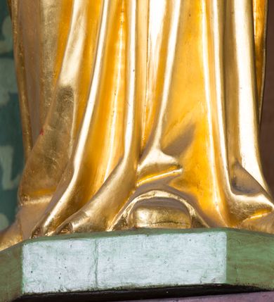 Zdjęcie nr 32: Kamienny ołtarz w jawiszowickim kościele uzyskał kształt prostopadłościanu. Otacza go drewniana obudowa podtrzymująca drewnianą mensę z portatylem. Jego przód zdobi drewniane antepedium ujęte profilowaną ramą z centralnym medalionem z monogramem Marii, otoczonym przez ornament roślinny. Ponad ołtarzem rozpościera się dwukondygnacyjna, architektoniczna nastawa ołtarzowa, flankowana przez dwie bramki. Struktura ołtarza dekorowana jest ciemnozieloną marmoryzacją. Pierwsza kondygnacja retabulum uzyskała trójosiowe założenie wsparte na dwustrefowym cokole, podzielonym płycinami z dekoracją akantową. Artykułują ją dwie pary kolumn o skręconych trzonach i kapitelach kompozytowych. Złocone w całości kolumny podtrzymują belkowanie o wysuniętym gzymsie, wyłamane na ich osi oraz przerwany trójkątny przyczółek. Pole środkowe nastawy wypełnia w całości nisza ujęta profilowaną, złoconą ramą w formie stojącego prostokąta zamkniętego trzema bokami z ośmioboku. W jej wnętrzu znajduje się obraz Matki Boskiej z Dzieciątkiem w typie Matki Boskiej Śnieżnej, zdobiony drewnianą złoconą i srebrzoną sukienką wotywną oraz koronami, a także dwie zasuwy z przedstawieniem św. Marcina, biskupa oraz bł. Salomei. Niszę środkową flankują znajdujące się pomiędzy kolumnami wąskie płyciny zwieńczone konchami. Na ich tle ustawiono figury św. Piotra i św. Pawła. Ponad nimi widoczne są na belkowaniu płaskorzeźbione i złocone girlandy kwiatowe oraz rozety. Na przerwanym przyczółku umieszczono dwie figury siedzących aniołów. Na mensie ołtarza centralnie ustawiono prostopadłościenne tabernakulum w drewnianej obudowie ujęte dwiema kolumienkami kompozytowymi o skręconych trzonach podtrzymujących belkowanie, do którego przymocowano świeczniki na sakramentki. Umieszczony na jego szczycie prosty tron eucharystyczny bez zaplecka flankują dwie figury uskrzydlonych aniołków. Drugą, jednoosiową kondygnację nastawy ujmuje także para złoconych kolumn o skręconych trzonach i kapitelach kompozytowych, ustawionych na cokołach, dźwigających imposty. Pomiędzy kolumnami nad polem z obrazem Wniebowzięcia Matki Boskiej widoczny jest wysunięty fragment gzymsu. Obraz ujęty został złoconą i profilowaną ramą w formie kwadratu o ściętych narożach. Po bokach obrazu na płycinie rozmieszczono złocone dekoracje akantowe. W zwieńczeniu na belkowaniu usytuowano dwa putta flankujące rzeźbę apokaliptycznego baranka leżącego na księdze. Obie kondygnacje ujmują uszaki z akantu suchego. Po bokach nastawy usytuowano dwie bramki flankowane pilastrami. Ich zwężające się ku dołowi trzony podtrzymują nadwieszony łuk półkolisty. Całość zamyka gzyms z centralnie usytuowanym cokołem, na którym stoją figury św. Stanisława i św. Wojciecha. Po ich bokach figur przy ścianach ustawiono rzeźbione i złocone wazony z kwiatami. 