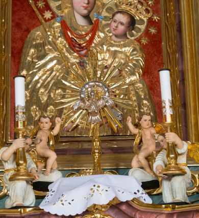 Zdjęcie nr 14: Kamienny ołtarz w jawiszowickim kościele uzyskał kształt prostopadłościanu. Otacza go drewniana obudowa podtrzymująca drewnianą mensę z portatylem. Jego przód zdobi drewniane antepedium ujęte profilowaną ramą z centralnym medalionem z monogramem Marii, otoczonym przez ornament roślinny. Ponad ołtarzem rozpościera się dwukondygnacyjna, architektoniczna nastawa ołtarzowa, flankowana przez dwie bramki. Struktura ołtarza dekorowana jest ciemnozieloną marmoryzacją. Pierwsza kondygnacja retabulum uzyskała trójosiowe założenie wsparte na dwustrefowym cokole, podzielonym płycinami z dekoracją akantową. Artykułują ją dwie pary kolumn o skręconych trzonach i kapitelach kompozytowych. Złocone w całości kolumny podtrzymują belkowanie o wysuniętym gzymsie, wyłamane na ich osi oraz przerwany trójkątny przyczółek. Pole środkowe nastawy wypełnia w całości nisza ujęta profilowaną, złoconą ramą w formie stojącego prostokąta zamkniętego trzema bokami z ośmioboku. W jej wnętrzu znajduje się obraz Matki Boskiej z Dzieciątkiem w typie Matki Boskiej Śnieżnej, zdobiony drewnianą złoconą i srebrzoną sukienką wotywną oraz koronami, a także dwie zasuwy z przedstawieniem św. Marcina, biskupa oraz bł. Salomei. Niszę środkową flankują znajdujące się pomiędzy kolumnami wąskie płyciny zwieńczone konchami. Na ich tle ustawiono figury św. Piotra i św. Pawła. Ponad nimi widoczne są na belkowaniu płaskorzeźbione i złocone girlandy kwiatowe oraz rozety. Na przerwanym przyczółku umieszczono dwie figury siedzących aniołów. Na mensie ołtarza centralnie ustawiono prostopadłościenne tabernakulum w drewnianej obudowie ujęte dwiema kolumienkami kompozytowymi o skręconych trzonach podtrzymujących belkowanie, do którego przymocowano świeczniki na sakramentki. Umieszczony na jego szczycie prosty tron eucharystyczny bez zaplecka flankują dwie figury uskrzydlonych aniołków. Drugą, jednoosiową kondygnację nastawy ujmuje także para złoconych kolumn o skręconych trzonach i kapitelach kompozytowych, ustawionych na cokołach, dźwigających imposty. Pomiędzy kolumnami nad polem z obrazem Wniebowzięcia Matki Boskiej widoczny jest wysunięty fragment gzymsu. Obraz ujęty został złoconą i profilowaną ramą w formie kwadratu o ściętych narożach. Po bokach obrazu na płycinie rozmieszczono złocone dekoracje akantowe. W zwieńczeniu na belkowaniu usytuowano dwa putta flankujące rzeźbę apokaliptycznego baranka leżącego na księdze. Obie kondygnacje ujmują uszaki z akantu suchego. Po bokach nastawy usytuowano dwie bramki flankowane pilastrami. Ich zwężające się ku dołowi trzony podtrzymują nadwieszony łuk półkolisty. Całość zamyka gzyms z centralnie usytuowanym cokołem, na którym stoją figury św. Stanisława i św. Wojciecha. Po ich bokach figur przy ścianach ustawiono rzeźbione i złocone wazony z kwiatami. 