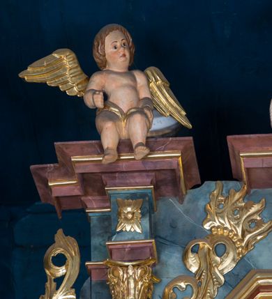 Zdjęcie nr 41: Kamienny ołtarz w jawiszowickim kościele uzyskał kształt prostopadłościanu. Otacza go drewniana obudowa podtrzymująca drewnianą mensę z portatylem. Jego przód zdobi drewniane antepedium ujęte profilowaną ramą z centralnym medalionem z monogramem Marii, otoczonym przez ornament roślinny. Ponad ołtarzem rozpościera się dwukondygnacyjna, architektoniczna nastawa ołtarzowa, flankowana przez dwie bramki. Struktura ołtarza dekorowana jest ciemnozieloną marmoryzacją. Pierwsza kondygnacja retabulum uzyskała trójosiowe założenie wsparte na dwustrefowym cokole, podzielonym płycinami z dekoracją akantową. Artykułują ją dwie pary kolumn o skręconych trzonach i kapitelach kompozytowych. Złocone w całości kolumny podtrzymują belkowanie o wysuniętym gzymsie, wyłamane na ich osi oraz przerwany trójkątny przyczółek. Pole środkowe nastawy wypełnia w całości nisza ujęta profilowaną, złoconą ramą w formie stojącego prostokąta zamkniętego trzema bokami z ośmioboku. W jej wnętrzu znajduje się obraz Matki Boskiej z Dzieciątkiem w typie Matki Boskiej Śnieżnej, zdobiony drewnianą złoconą i srebrzoną sukienką wotywną oraz koronami, a także dwie zasuwy z przedstawieniem św. Marcina, biskupa oraz bł. Salomei. Niszę środkową flankują znajdujące się pomiędzy kolumnami wąskie płyciny zwieńczone konchami. Na ich tle ustawiono figury św. Piotra i św. Pawła. Ponad nimi widoczne są na belkowaniu płaskorzeźbione i złocone girlandy kwiatowe oraz rozety. Na przerwanym przyczółku umieszczono dwie figury siedzących aniołów. Na mensie ołtarza centralnie ustawiono prostopadłościenne tabernakulum w drewnianej obudowie ujęte dwiema kolumienkami kompozytowymi o skręconych trzonach podtrzymujących belkowanie, do którego przymocowano świeczniki na sakramentki. Umieszczony na jego szczycie prosty tron eucharystyczny bez zaplecka flankują dwie figury uskrzydlonych aniołków. Drugą, jednoosiową kondygnację nastawy ujmuje także para złoconych kolumn o skręconych trzonach i kapitelach kompozytowych, ustawionych na cokołach, dźwigających imposty. Pomiędzy kolumnami nad polem z obrazem Wniebowzięcia Matki Boskiej widoczny jest wysunięty fragment gzymsu. Obraz ujęty został złoconą i profilowaną ramą w formie kwadratu o ściętych narożach. Po bokach obrazu na płycinie rozmieszczono złocone dekoracje akantowe. W zwieńczeniu na belkowaniu usytuowano dwa putta flankujące rzeźbę apokaliptycznego baranka leżącego na księdze. Obie kondygnacje ujmują uszaki z akantu suchego. Po bokach nastawy usytuowano dwie bramki flankowane pilastrami. Ich zwężające się ku dołowi trzony podtrzymują nadwieszony łuk półkolisty. Całość zamyka gzyms z centralnie usytuowanym cokołem, na którym stoją figury św. Stanisława i św. Wojciecha. Po ich bokach figur przy ścianach ustawiono rzeźbione i złocone wazony z kwiatami. 