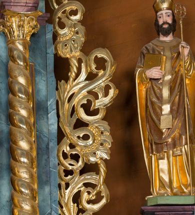 Zdjęcie nr 28: Kamienny ołtarz w jawiszowickim kościele uzyskał kształt prostopadłościanu. Otacza go drewniana obudowa podtrzymująca drewnianą mensę z portatylem. Jego przód zdobi drewniane antepedium ujęte profilowaną ramą z centralnym medalionem z monogramem Marii, otoczonym przez ornament roślinny. Ponad ołtarzem rozpościera się dwukondygnacyjna, architektoniczna nastawa ołtarzowa, flankowana przez dwie bramki. Struktura ołtarza dekorowana jest ciemnozieloną marmoryzacją. Pierwsza kondygnacja retabulum uzyskała trójosiowe założenie wsparte na dwustrefowym cokole, podzielonym płycinami z dekoracją akantową. Artykułują ją dwie pary kolumn o skręconych trzonach i kapitelach kompozytowych. Złocone w całości kolumny podtrzymują belkowanie o wysuniętym gzymsie, wyłamane na ich osi oraz przerwany trójkątny przyczółek. Pole środkowe nastawy wypełnia w całości nisza ujęta profilowaną, złoconą ramą w formie stojącego prostokąta zamkniętego trzema bokami z ośmioboku. W jej wnętrzu znajduje się obraz Matki Boskiej z Dzieciątkiem w typie Matki Boskiej Śnieżnej, zdobiony drewnianą złoconą i srebrzoną sukienką wotywną oraz koronami, a także dwie zasuwy z przedstawieniem św. Marcina, biskupa oraz bł. Salomei. Niszę środkową flankują znajdujące się pomiędzy kolumnami wąskie płyciny zwieńczone konchami. Na ich tle ustawiono figury św. Piotra i św. Pawła. Ponad nimi widoczne są na belkowaniu płaskorzeźbione i złocone girlandy kwiatowe oraz rozety. Na przerwanym przyczółku umieszczono dwie figury siedzących aniołów. Na mensie ołtarza centralnie ustawiono prostopadłościenne tabernakulum w drewnianej obudowie ujęte dwiema kolumienkami kompozytowymi o skręconych trzonach podtrzymujących belkowanie, do którego przymocowano świeczniki na sakramentki. Umieszczony na jego szczycie prosty tron eucharystyczny bez zaplecka flankują dwie figury uskrzydlonych aniołków. Drugą, jednoosiową kondygnację nastawy ujmuje także para złoconych kolumn o skręconych trzonach i kapitelach kompozytowych, ustawionych na cokołach, dźwigających imposty. Pomiędzy kolumnami nad polem z obrazem Wniebowzięcia Matki Boskiej widoczny jest wysunięty fragment gzymsu. Obraz ujęty został złoconą i profilowaną ramą w formie kwadratu o ściętych narożach. Po bokach obrazu na płycinie rozmieszczono złocone dekoracje akantowe. W zwieńczeniu na belkowaniu usytuowano dwa putta flankujące rzeźbę apokaliptycznego baranka leżącego na księdze. Obie kondygnacje ujmują uszaki z akantu suchego. Po bokach nastawy usytuowano dwie bramki flankowane pilastrami. Ich zwężające się ku dołowi trzony podtrzymują nadwieszony łuk półkolisty. Całość zamyka gzyms z centralnie usytuowanym cokołem, na którym stoją figury św. Stanisława i św. Wojciecha. Po ich bokach figur przy ścianach ustawiono rzeźbione i złocone wazony z kwiatami. 