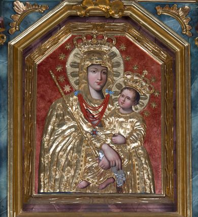 Zdjęcie nr 2: Obraz Matki Boskiej Jawiszowickiej ma formę stojącego prostokąta zamkniętego trzema bokami z ośmioboku. Widoczne spod sukienki wotywnej twarze, ręce i nóżki Dzieciątka malowane są na desce, resztę przykrywa złocona i rzeźbiona drewniana sukienka. Obraz przedstawia w półpostaci Matkę Boską zwróconą nieznacznie w trzech czwartych w lewo, trzymającą na lewym ramieniu Dzieciątko. Maria małego Jezusa podtrzymuje obiema, skrzyżowanymi rękami. Równocześnie w lewej dłoni trzyma płaskorzeźbione berło, będące elementem sukienki wotywnej, a w prawej podobnie zaaranżowaną chustkę. Jej twarz jest pociągła o delikatnych, łagodnych rysach, z prostym nosem i pełnych ustach, o jasnej karnacji modelowanej miękkim światłocieniem. Na głowie ma lamowany maforion opadający na ramiona i odsłaniający spodnią suknię. Maforion zdobiony jest płaskorzeźbionymi różyczkami na łodyżce z podwójnymi listkami. Dzieciątko jest zwrócone trzy czwarte w prawo, lewą ręka podtrzymuje przy boku księgę Ewangelii. Natomiast nieznacznie usztywnioną i wyciągniętą przed siebie prawą rękę unosi w geście błogosławieństwa. Jezus ma okrągłą twarz o jasnej karnacji, pełnych ustach i rumianych policzkach, okoloną jasnobrązowymi, krótkimi włosami. Ubrany jest w tunikę o wzorze w drobne kwiatki z lamówką. Na głowach obojga widoczne są korony zamknięte, wokół nich nimby i wieńce z gwiazd. Postacie ukazane zostały na jednolitym, czerwonym tle. Pod szyją Matki Boskiej wisi przytwierdzony do sukienki wotywnej sznur korali.
