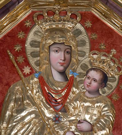 Zdjęcie nr 4: Obraz Matki Boskiej Jawiszowickiej ma formę stojącego prostokąta zamkniętego trzema bokami z ośmioboku. Widoczne spod sukienki wotywnej twarze, ręce i nóżki Dzieciątka malowane są na desce, resztę przykrywa złocona i rzeźbiona drewniana sukienka. Obraz przedstawia w półpostaci Matkę Boską zwróconą nieznacznie w trzech czwartych w lewo, trzymającą na lewym ramieniu Dzieciątko. Maria małego Jezusa podtrzymuje obiema, skrzyżowanymi rękami. Równocześnie w lewej dłoni trzyma płaskorzeźbione berło, będące elementem sukienki wotywnej, a w prawej podobnie zaaranżowaną chustkę. Jej twarz jest pociągła o delikatnych, łagodnych rysach, z prostym nosem i pełnych ustach, o jasnej karnacji modelowanej miękkim światłocieniem. Na głowie ma lamowany maforion opadający na ramiona i odsłaniający spodnią suknię. Maforion zdobiony jest płaskorzeźbionymi różyczkami na łodyżce z podwójnymi listkami. Dzieciątko jest zwrócone trzy czwarte w prawo, lewą ręka podtrzymuje przy boku księgę Ewangelii. Natomiast nieznacznie usztywnioną i wyciągniętą przed siebie prawą rękę unosi w geście błogosławieństwa. Jezus ma okrągłą twarz o jasnej karnacji, pełnych ustach i rumianych policzkach, okoloną jasnobrązowymi, krótkimi włosami. Ubrany jest w tunikę o wzorze w drobne kwiatki z lamówką. Na głowach obojga widoczne są korony zamknięte, wokół nich nimby i wieńce z gwiazd. Postacie ukazane zostały na jednolitym, czerwonym tle. Pod szyją Matki Boskiej wisi przytwierdzony do sukienki wotywnej sznur korali.
