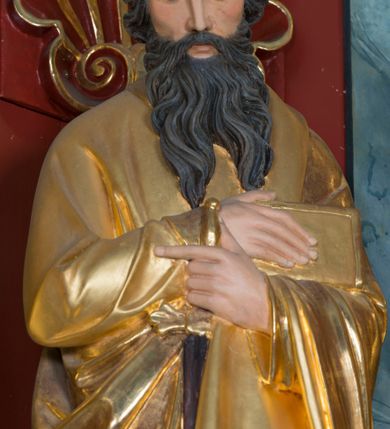 Zdjęcie nr 4: Pełnoplastyczna rzeźba św. Pawła Apostoła została ustawiona na zielonej podstawie na planie kwadratu o ściętych narożach. Święty został ukazany frontalnie w całej postaci. Apostoł ma nieznacznie pochyloną głowę do przodu i ręce skrzyżowane na piersi. Prawą podtrzymuję księgę wspartą o lewe przedramię, trzymając jednocześnie w lewej miecz, skierowany ostrzem ku ziemi. Święty Paweł ma pociągłą twarz okoloną czarnymi włosami i rozdwojoną, długą brodę. Jego spojrzenie skierowane jest w dół. Ma prosty nos, wyraziste oczy i usta. Ubrany jest w przylegającą do ciała tunikę oraz płaszcz narzucony na lewe ramię i podtrzymywany z przodu. Spod tuniki widoczne są bose stopy. W partiach ciała widoczna jest polichromia naturalistyczna. Natomiast szaty i atrybuty są złocone. 