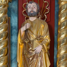 Zdjęcie nr 1: Pełnoplastyczna rzeźba ustawiona na zielonej podstawie na planie kwadratu o ściętych narożach przedstawia św. Piotra Apostoła. Święty został ukazany frontalnie w nieznacznym kontrapoście z prawą ręką uniesioną na wysokość piersi, w której trzyma zawieszone na łańcuszku dwa złote klucze. Lewą ręką podtrzymuje połę płaszcza oraz księgę przyciśnięte do ciała powyżej bioder. Apostoł ma owalną twarz o wyrazistych rysach, otoczoną kędzierzawym, krótkim szpakowatym zarostem i włosami. Jego spojrzenie skierowane jest przed siebie. Ma prosty nos i wydatne usta. Ubrany jest w przylegającą do ciała tunikę oraz płaszcz narzucony na prawe ramię i podtrzymywany z przodu. Spod tuniki widoczne są obute w sandały bose stopy. Obie szaty są silnie drapowane. W partiach ciała widoczna jest naturalistyczna polichromia. Natomiast ubranie i atrybuty zostały wyzłocone.