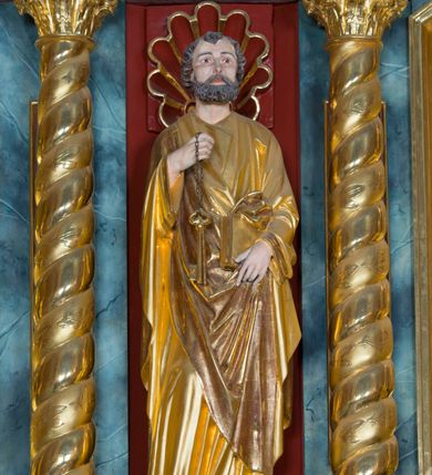 Zdjęcie nr 4: Pełnoplastyczna rzeźba ustawiona na zielonej podstawie na planie kwadratu o ściętych narożach przedstawia św. Piotra Apostoła. Święty został ukazany frontalnie w nieznacznym kontrapoście z prawą ręką uniesioną na wysokość piersi, w której trzyma zawieszone na łańcuszku dwa złote klucze. Lewą ręką podtrzymuje połę płaszcza oraz księgę przyciśnięte do ciała powyżej bioder. Apostoł ma owalną twarz o wyrazistych rysach, otoczoną kędzierzawym, krótkim szpakowatym zarostem i włosami. Jego spojrzenie skierowane jest przed siebie. Ma prosty nos i wydatne usta. Ubrany jest w przylegającą do ciała tunikę oraz płaszcz narzucony na prawe ramię i podtrzymywany z przodu. Spod tuniki widoczne są obute w sandały bose stopy. Obie szaty są silnie drapowane. W partiach ciała widoczna jest naturalistyczna polichromia. Natomiast ubranie i atrybuty zostały wyzłocone.