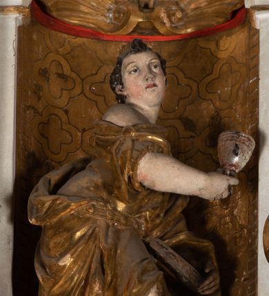 Zdjęcie nr 12: Epitafium uzyskało formę jednokondygnacyjnej, trójosiowej struktury architektonicznej z podstawą i zwieńczeniem, flankowanej po bokach fantazyjnymi uszakami. Część środkową tworzą trzy aedicule rozdzielone dwiema złoconymi kolumnami o korynckich kapitelach i trzonach dekorowanych festonami, a w dolnych partiach pierścieniami. Kolumny podtrzymują pełne belkowanie przechodzące przez całą szerokości kondygnacji, wyłamane nad osiami bocznymi. Same zaś stoją na cokole, który stanowi równocześnie wyłamany gzyms dla podstawy. Pole osi środkowej otrzymało kształt aediculi w formie stojącego prostokąta ze schodkowym zamknięciem u góry, wypełnionym ażurowym, złoconym maswerkiem. Jej wnętrze wypełnia płaskorzeźbione słońce pośród chmur na malowanym tle nieba. Poniżej ukazano panoramę Jerozolimy. Przed aediculą ustawiono na postumencie drewniany krzyż. Na osiach bocznych znalazły się nisze zwieńczone złotymi muszlami oraz złoconą, rytą ornamentyką z motywem czteroliścia. Pierwotnie znajdowały się tu rzeźby Mojżesza i Jana Chrzciciela. Całość po bokach flankują fantazyjne uszaki utworzone ornamentu rollwerkowego oraz z widocznych z profilu półpostaci maurów podtrzymujących belkowanie. Pole uszaków wypełniają pionowo ułożone owalne kartusze o czerwonych polach, stanowiące tło dla dwóch par tarczy herbowych z klejnotami. Z lewej umieszczono herb Dołęga, a z prawej herb Jastrzębiec (bez klejnotu). Po zewnętrznych stronach na belkowaniu ustawiono dwa półsiedzące uskrzydlone anioły (zachował się tylko anioł z prawej strony). Jednocześnie postacie aniołów flankują zwieńczenie epitafium, które tworzy aedicula wypełniona złotą muszlą oraz rytym złoconym ornamentem z motywem czteroliścia. Flankują ją dwa pilastry podtrzymujące wyłamane belkowanie na ich osi. W aediculi ustawiono pełnoplastyczną rzeźbę stojącej kobiety. Została ona ukazana w wydatnym kontrapoście z tułowiem skręconym w lewo, z głową ujętą w trzech czwartych w prawo. Kobieta w podniesionej prawej ręce trzyma srebrny kielich, natomiast w opuszczonej i wspartej o wysuniętą tanecznie lewą nogę otwartą księgę. Postać ma owalną twarz o jasnej karnacji i rumianych policzkach z prostym nosem i wydatnymi ustami. Jej głowę otaczają falujące, brązowe włosy opadające na plecy i  odsłaniające uszy. Ubrana jest w złoconą, mocno drapowaną suknię, która odsłania wysuniętą nogę. Po bokach pilastrów widoczne są dwa uszaki. Na szczycie zwieńczenia dwa pulchne putta prezentują chustę Weroniki, która została równocześnie przytwierdzona do wysokiego impostu wspierającego ażurowy, złocony kwiaton. Na chuście wyobrażono płaskorzeźbioną głowę Chrystusa w cierniowej koronie. Zbawiciel ma owalną twarz z szeroko otwartymi oczami, wydatnym nosem i półotwartymi ustami. Otaczają ją kręcone brązowe włosy oraz podobna, krótka broda. Podstawę epitafium tworzy wykrojona po bokach struktura, w której centrum umieszczono fantazyjnie wyciętą drewnianą, czarną tablicę ze złotym łacińskim napisem "O HOMO FVI QVOD ES SVM QVOD ERIS / NVNC DE(M)VM VIVERE CO(E)PI, MORI DESII, VITA MIHI / PRIOR MORTE(M), MORS PRIA(M) VITA(M) SECV(N)DA(M), QVAE NU(N) QVA(M) / EST I(N)TERI TVRA DEDIT, MO(R)TALITATES  MEOR, HO(C) MIHI / EST ET VXORI MO(S) VENTV(S) POSVI, VIPOST QV(E)ALETHIVERA DVCEDI / NELVSOS, ET CARNIS EXVVIIS SO(L)VTOS  ABHOC PELAG  SECVRA / GLAVSTRA SVB IRE IVABIT, HIC MORTALE DIMIDIVM N(OST)RI, IMMORTA/LE(M) EXPECT ET IM(M)ORTALITATEM, E QVOS VITA CONIVCTOS TENVIT / MORS IDIVISOS CVSTODIRET, SI PIVS ES, PIAS PRECES ADDE, ET / HIC HV(M)O SVB HVMO QVIETA[M], ANIMAE IN COELESTI PATRIA / LETAM  QVIETEM APPRECARE "NICOLAVS CORNITIVS DE / MAGNA POREMBA ET BEATA DE MIROW CONSOR/TES SE(M)PER VAIESL[?]" / A(NNO) D(OMINI) 1611 P(ATRONVS) P(OSVIT)". Tablicę umieszczono w kartuszu rollwerkowym pomiędzy dwiema konsolami zdobionymi pierwotnie uskrzydlonymi główkami aniołków, podtrzymującymi belkowanie z krzyżem. Poniżej tablicy zastosowano odwrócony łuk odcinkowy z podwieszonym kartuszem rollwerkowym zawieszonym na festonach. W jego wnętrzu przedstawiono tabliczkę z napisem „VITA FUGIT VT HORA”, a po niżej trupią czaszkę ze skrzyżowanymi piszczelami.  
