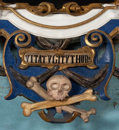 Zdjęcie nr 10: Epitafium uzyskało formę jednokondygnacyjnej, trójosiowej struktury architektonicznej z podstawą i zwieńczeniem, flankowanej po bokach fantazyjnymi uszakami. Część środkową tworzą trzy aedicule rozdzielone dwiema złoconymi kolumnami o korynckich kapitelach i trzonach dekorowanych festonami, a w dolnych partiach pierścieniami. Kolumny podtrzymują pełne belkowanie przechodzące przez całą szerokości kondygnacji, wyłamane nad osiami bocznymi. Same zaś stoją na cokole, który stanowi równocześnie wyłamany gzyms dla podstawy. Pole osi środkowej otrzymało kształt aediculi w formie stojącego prostokąta ze schodkowym zamknięciem u góry, wypełnionym ażurowym, złoconym maswerkiem. Jej wnętrze wypełnia płaskorzeźbione słońce pośród chmur na malowanym tle nieba. Poniżej ukazano panoramę Jerozolimy. Przed aediculą ustawiono na postumencie drewniany krzyż. Na osiach bocznych znalazły się nisze zwieńczone złotymi muszlami oraz złoconą, rytą ornamentyką z motywem czteroliścia. Pierwotnie znajdowały się tu rzeźby Mojżesza i Jana Chrzciciela. Całość po bokach flankują fantazyjne uszaki utworzone ornamentu rollwerkowego oraz z widocznych z profilu półpostaci maurów podtrzymujących belkowanie. Pole uszaków wypełniają pionowo ułożone owalne kartusze o czerwonych polach, stanowiące tło dla dwóch par tarczy herbowych z klejnotami. Z lewej umieszczono herb Dołęga, a z prawej herb Jastrzębiec (bez klejnotu). Po zewnętrznych stronach na belkowaniu ustawiono dwa półsiedzące uskrzydlone anioły (zachował się tylko anioł z prawej strony). Jednocześnie postacie aniołów flankują zwieńczenie epitafium, które tworzy aedicula wypełniona złotą muszlą oraz rytym złoconym ornamentem z motywem czteroliścia. Flankują ją dwa pilastry podtrzymujące wyłamane belkowanie na ich osi. W aediculi ustawiono pełnoplastyczną rzeźbę stojącej kobiety. Została ona ukazana w wydatnym kontrapoście z tułowiem skręconym w lewo, z głową ujętą w trzech czwartych w prawo. Kobieta w podniesionej prawej ręce trzyma srebrny kielich, natomiast w opuszczonej i wspartej o wysuniętą tanecznie lewą nogę otwartą księgę. Postać ma owalną twarz o jasnej karnacji i rumianych policzkach z prostym nosem i wydatnymi ustami. Jej głowę otaczają falujące, brązowe włosy opadające na plecy i  odsłaniające uszy. Ubrana jest w złoconą, mocno drapowaną suknię, która odsłania wysuniętą nogę. Po bokach pilastrów widoczne są dwa uszaki. Na szczycie zwieńczenia dwa pulchne putta prezentują chustę Weroniki, która została równocześnie przytwierdzona do wysokiego impostu wspierającego ażurowy, złocony kwiaton. Na chuście wyobrażono płaskorzeźbioną głowę Chrystusa w cierniowej koronie. Zbawiciel ma owalną twarz z szeroko otwartymi oczami, wydatnym nosem i półotwartymi ustami. Otaczają ją kręcone brązowe włosy oraz podobna, krótka broda. Podstawę epitafium tworzy wykrojona po bokach struktura, w której centrum umieszczono fantazyjnie wyciętą drewnianą, czarną tablicę ze złotym łacińskim napisem "O HOMO FVI QVOD ES SVM QVOD ERIS / NVNC DE(M)VM VIVERE CO(E)PI, MORI DESII, VITA MIHI / PRIOR MORTE(M), MORS PRIA(M) VITA(M) SECV(N)DA(M), QVAE NU(N) QVA(M) / EST I(N)TERI TVRA DEDIT, MO(R)TALITATES  MEOR, HO(C) MIHI / EST ET VXORI MO(S) VENTV(S) POSVI, VIPOST QV(E)ALETHIVERA DVCEDI / NELVSOS, ET CARNIS EXVVIIS SO(L)VTOS  ABHOC PELAG  SECVRA / GLAVSTRA SVB IRE IVABIT, HIC MORTALE DIMIDIVM N(OST)RI, IMMORTA/LE(M) EXPECT ET IM(M)ORTALITATEM, E QVOS VITA CONIVCTOS TENVIT / MORS IDIVISOS CVSTODIRET, SI PIVS ES, PIAS PRECES ADDE, ET / HIC HV(M)O SVB HVMO QVIETA[M], ANIMAE IN COELESTI PATRIA / LETAM  QVIETEM APPRECARE "NICOLAVS CORNITIVS DE / MAGNA POREMBA ET BEATA DE MIROW CONSOR/TES SE(M)PER VAIESL[?]" / A(NNO) D(OMINI) 1611 P(ATRONVS) P(OSVIT)". Tablicę umieszczono w kartuszu rollwerkowym pomiędzy dwiema konsolami zdobionymi pierwotnie uskrzydlonymi główkami aniołków, podtrzymującymi belkowanie z krzyżem. Poniżej tablicy zastosowano odwrócony łuk odcinkowy z podwieszonym kartuszem rollwerkowym zawieszonym na festonach. W jego wnętrzu przedstawiono tabliczkę z napisem „VITA FUGIT VT HORA”, a po niżej trupią czaszkę ze skrzyżowanymi piszczelami.  
