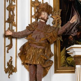 Zdjęcie nr 1: Ustawiona na cokole o nieregularnym planie, pełnoplastyczna rzeźba drążona, ukazuje anonimowego świętego króla. Figura zwrócona jest do widza frontalnie, z głową i torsem wychylonym w lewo i skierowanymi w układzie trzech czwartych. Król stoi w kontrapoście z rękami rozłożonymi na boki. Jest to dojrzały mężczyzna o szczupłej twarzy i podkreślonych kościach policzkowych i linii łuków brwiowych. Charakteryzuje się silnie zadartym, wąskim nosem, pełnymi i lekko rozchylonymi wargami. Jego niewielkie, okrągłe oczy skierowane są w górę. Twarz okala silnie skręcona w dwa pukle broda oraz krótkie, kręcone włosy. Monarcha ubrany jest w tunikę lamowaną frędzlą i sięgającą kolan. Na niej nałożony ma pancerz lekkiej zbroi płytowej z zarękawiami przewiązany w pasie szarfą, za którą ma wetknięte dwie gałązki palmowe. Jego nogi ochraniają nadgolennice i trzewiki. Na ramionach ma narzucony płaszcz podbity gronostajem, zapięty na piersi, którego poły rozwiewają się po bokach postaci. Jego głowę zdobi zamknięta korona o stylizowanych sterczynach. Partie odsłoniętego ciała pokrywa naturalistyczna polichromia, natomiast korona i płaszcz są złocone, a elementy zbroi srebrzone.