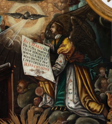 Zdjęcie nr 11: Obraz uzyskał formę stojącego prostokąta zamkniętego u góry łukiem odcinkowym nadwieszonym z uskokami, ujętego profilowaną ramą. W środkowej części kompozycji przedstawiono scenę zwiastowania Najświętszej Marii Pannie.
Marię ujętą w trzech czwartych w prawo wyobrażono klęczącą na klęczniku z lewej strony kompozycji. Lewą rękę przycisk do piersi, a prawą nieznacznie odsuwa od siebie. Jest to młoda dziewczyna po owalnej twarzy z jasną karnacją, wydatnym nosem i ustami z mocno drapowaną białą chusta na głowie zakrywającą jest włosy. Głowę Marii okala nimb. Madonna ubrań jest w bladofioletową suknię oraz ciemnozielony płaszcz nieznacznie zsuwający się z jej prawego ramienia, którego poła okrywa jej kolana. Na drewnianym klęczniku leży otwarta księga. Klęczący przed nią uskrzydlony Archanioł Gabriel ujęty w trzech czwartych w lewo klęczy na szarobiałych obłokach. Obiema rękami prezentuje Marii pergaminowy list zakończony u dołu zawieszoną na przytwierdzonych do jego rogów sznurku okrągłą, woskową pieczęcią zdobioną symbolem Trójcy Świętej. Na liście umieszczono kaligraficzne wypisane pozdrowienie anielskie: „AVE MARIA GRA/TIA PLENA DOMINVS / TECVM BENEDICTA TV / IN MVLIERIBVS ET / BENEDICTVS TRV/CTVS [FRVCTVS] VENTRIS TVI / JESVS CHRISTVS”. Jego młodzieńcza twarz o jasnej karnacji z wydatnym nosem i ustami widoczna jest z profilu. Otaczają ją falujące brązowe włosy, spływające na jego plecy spod złotego diademu dekorowanego na przędzie klejnotem z krzyżykiem. Gabriel ubrany jest w jasną tunikę dekorowaną drobnymi kwiatuszkami oraz złocistą szatę z podwiniętymi rękawami opadającą na jego plecy i przewiązaną skrzyżowaną na piersi ciemnozieloną stułą o końcach zdobionych złotymi chwostami. Pomiędzy obłokami na których klęczy archanioł widoczne są uskrzydlone główki anielskie. W górnej części kompozycji widać otwarte niebiosa okolone po zewnętrznej niebieskoszarymi obłokami z igrającymi w nich aniołkami adorującymi widocznego w połowie na obłoku Boga Ojca. Stworzyciel został ukazany na jasnym tle utworzonym z niezliczonej liczby ułożonych koncentrycznie uskrzydlonych główek anielskich. Bóg Ojciec został ujęty frontalnie z uniesioną prawą ręką oraz niebieskim globem podtrzymywanym lewą na szaroniebieskim obłoku. Jest to starzec z obfitą siwą brodą i włosami oraz zamkniętymi oczami. Ubrany jest w ciemnoniebieską tunikę oraz przerzucony prze lewe ramię bladoszkarłatny płaszcz. Poniże ponad głowami Marii i Archanioła w świetlanym otoku przedstawiono gołębicę Ducha Świętego, od której snop świtała pada na Marię. W dolnej części kompozycji wyobrażono siedzących sześciu proroków i królów starotestamentalnych trzymających prostokątne tablice z napisami. Widoczny w centrum król Dawid gra na złocistej harfie. Są to starsi mężczyźni w orientalnych strojach. Dwóch z nich ma złote korony, dwóch wzorzyste turbany, a dwaj pozostali mają głowy okryte tkaninami. Ich twarze okalają siwe brody, bądź też krótkie brody brązowe. W prawym dolnym rogu widoczna jest sygnatura „B. Weiss 1896.”