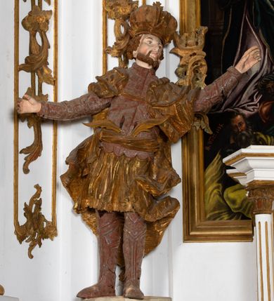 Zdjęcie nr 16: Kamienny ołtarz zamknięto w drewnianej obudowie, nakrywając go  drewnianą mensą z portatylem. Stipes ołtarzowy uzyskał kształt prostopadłościanu. Jego przód zdobi drewniane antepedium ujęte profilowaną ramą z malowanym chrystogramem "IHS" w glorii w polu. Na mensie ołtarza usytuowano tabernakulum w formie stojącego prostopadłościanu o wypukłym froncie i wklęsłych bokach wspierającego się na cokole. Jego przód ujmuje para kolumn podtrzymujących niepełne belkowanie, wyłamane nad ścianą frontową na kształt łuku odcinkowego nadwieszonego. Na froncie zamontowano obrotową, dwustronną niszę ujętą ramą w formie stojącego prostokąta zamkniętego łukiem półkolistym, wielolistnym. Nisze bębna zwieńczone zostały złoconymi konchami. Na tabernakulum usytuowano tron eucharystyczny w formie cokołu z leżącą księgą o siedmiu pieczęciach w glorii. Retabulum ołtarzowe wzniesiono na planie półowalu i polichromowano je na biało. Jest to architektoniczna, jednokondygnacyjna, jednoosiowa struktura ze zwieńczeniem. Po bokach flankują ją bramki ustawione na dwustrefowym, tralkowym, wklęsło-wypukłym cokole. Kondygnacja została ujęta dwiema parami pilastrów zwróconych delikatnie do wewnątrz oraz silnie wysuniętą do przodu parą kolumn o kapitelach kompozytowych. Podpory dźwigają pełne belkowanie o wklęsło-wypukłej linii. Nad polem środkowym belkowanie jest połączone gzymsem przyjmującym formę łuku falistego i wyłamane na osiach podpór. Kondygnacje ujmują spływy wolutowe połączone z łukowato wygiętymi wolutami podtrzymywanymi przez wysokie tralkowe cokoły, tworząc bramki ołtarza. W polu środkowym umieszczono obraz Zwiastowania ujęty profilowaną, złoconą ramą w formie stojącego prostokąta zamkniętego łukiem półkolistym nadwieszonym z uskokiem. Zwieńczenie uzyskało formę leżącego prostokąta flankowanego parą pilastrów zwróconych do wewnątrz oraz parą pilastrów zwróconych na zewnątrz, których trzony przechodzą w spływy wolutowe opadające na belkowanie. Pilastry dźwigają niepełne, wklęsło-wypukłe belkowanie przyjmujące nad polem formę łuku falistego. Całość wieńczy kartusz rokokowy z chrystogramem "IHS". W polu zwieńczenia znalazł się obraz św. Andrzeja w profilowanej, złoconej ramie o fantazyjnej formie zbliżonej do stojącego prostokąta. Pilastry kondygnacji ozdobiono kapitelami z rocaille'ów, a ich trzony udekorowano złoconymi, rokokowymi panneau ze zwisami utworzonymi z rocaille'ów, rozet i liści. Na ich tle usytuowano figury świętego króla i św. Jana Chrzciciela. Rzeźby stoją na górnej strefie cokołu na wspornikach z rocaille. Na ramie obrazu w polu środkowym, w przyłuczach i na belkowaniu znalazły się ornamenty roślinne. Z kolei na wolutowych łukach bramek umieszczono rokokowe wazony oraz pary figur aniołów z kartuszami. Na belkowaniu i wolutach zwieńczenia znajdują się dwie pary puttów. Także trzony pilastrów zwieńczenia dekorowane są złoconymi zwisami z rocaille'ów i kwiatów. Pole wokół obrazu św. Andrzeja zostało ozdobione fragmentami rocaille'ów. Pod gzymsem koronującym powyżej obrazu, podwieszono lambrekin, zdobiony przy górnej krawędzi złoconymi liśćmi i rocaille'm. 